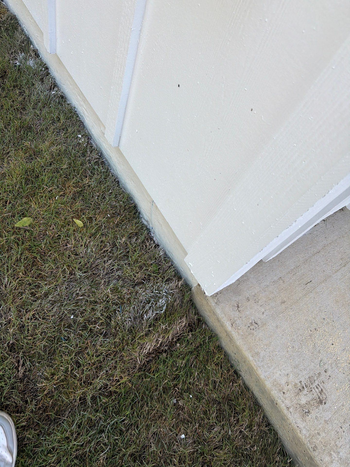 Corner of a white exterior wall beside a concrete path and grass lawn