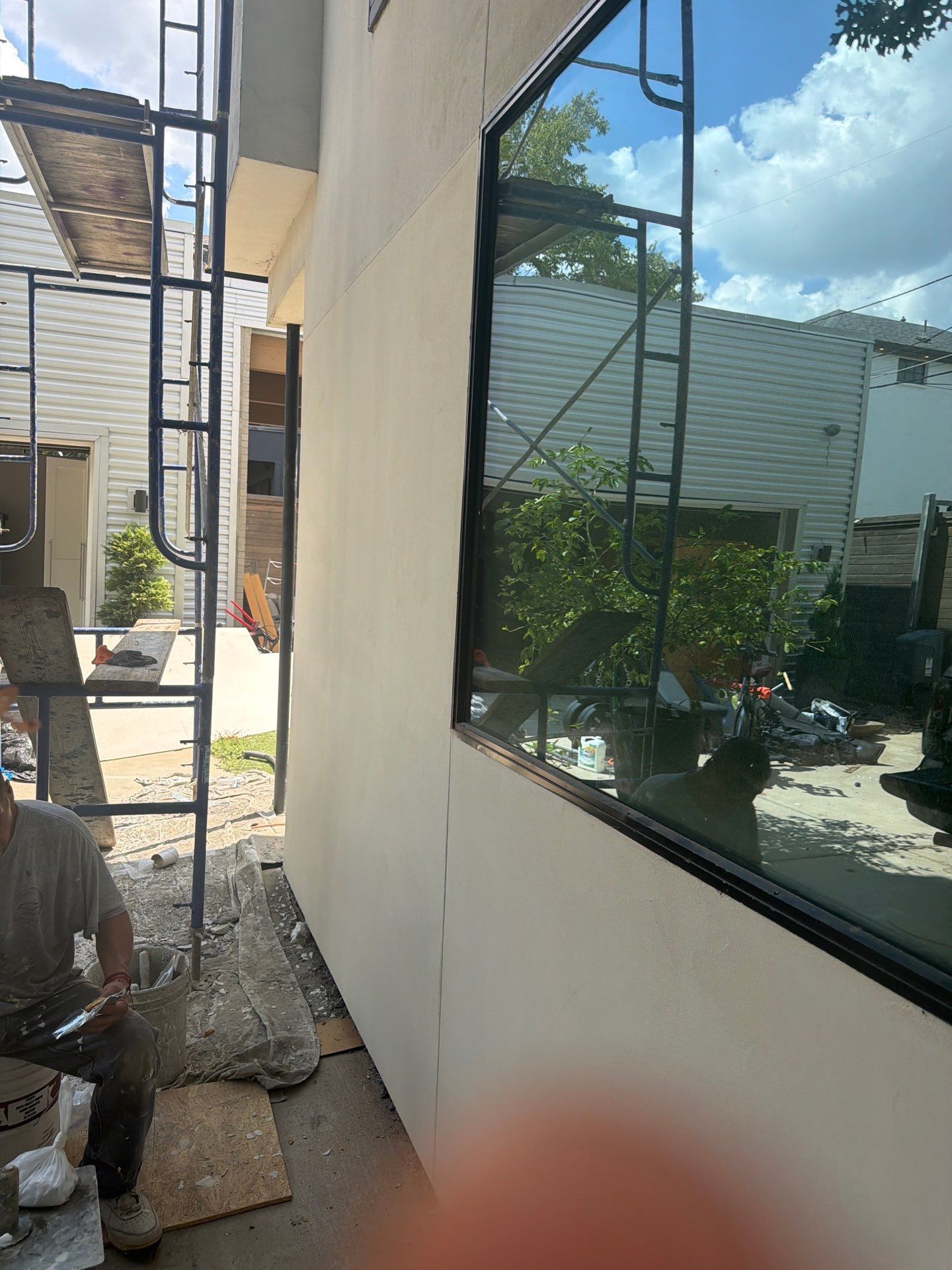 Narrow outdoor side yard with white walls, a large window, metal ladder, and a worker near the left edge.