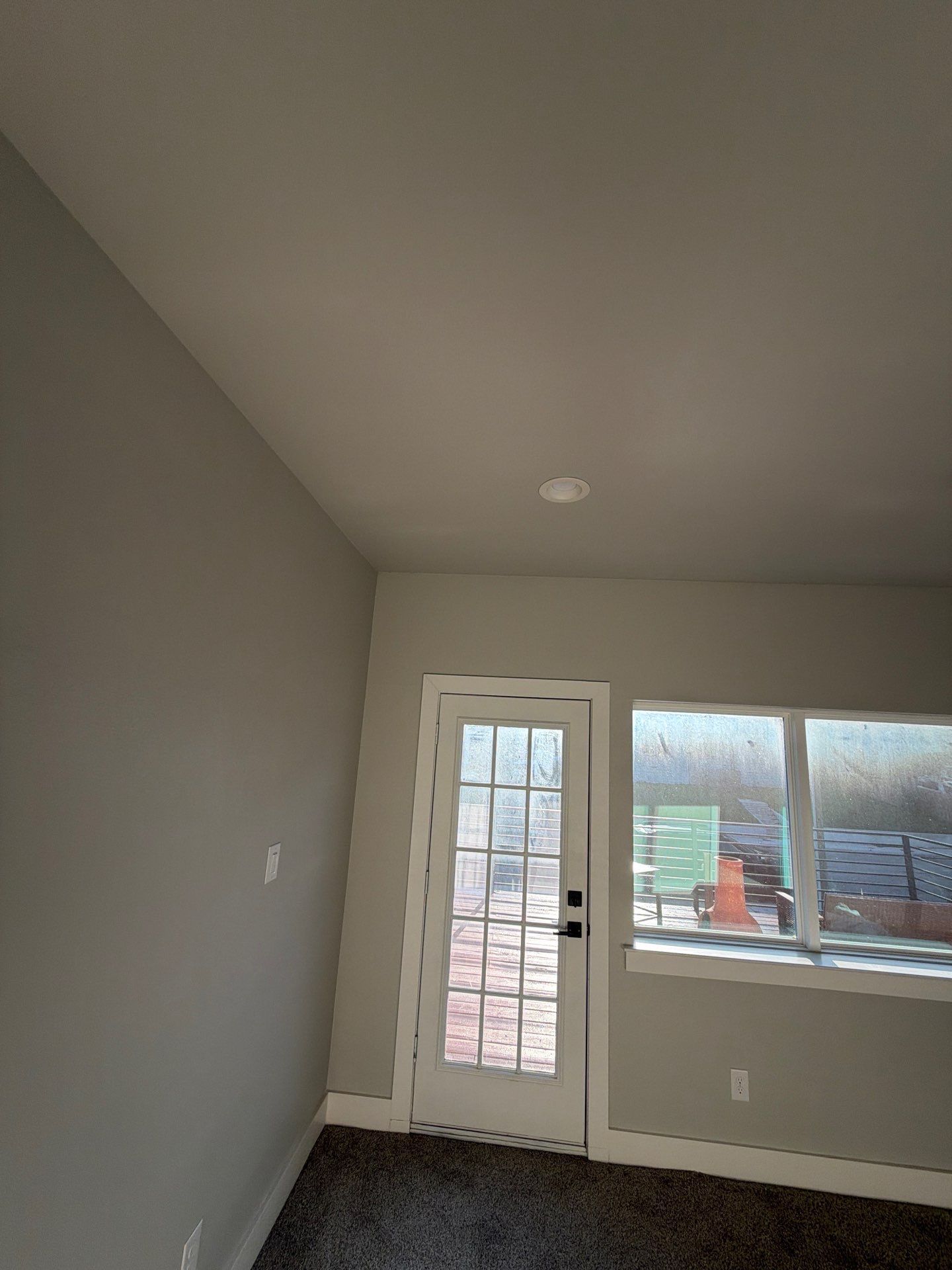 Empty gray room with a door to a deck and a window letting in daylight.