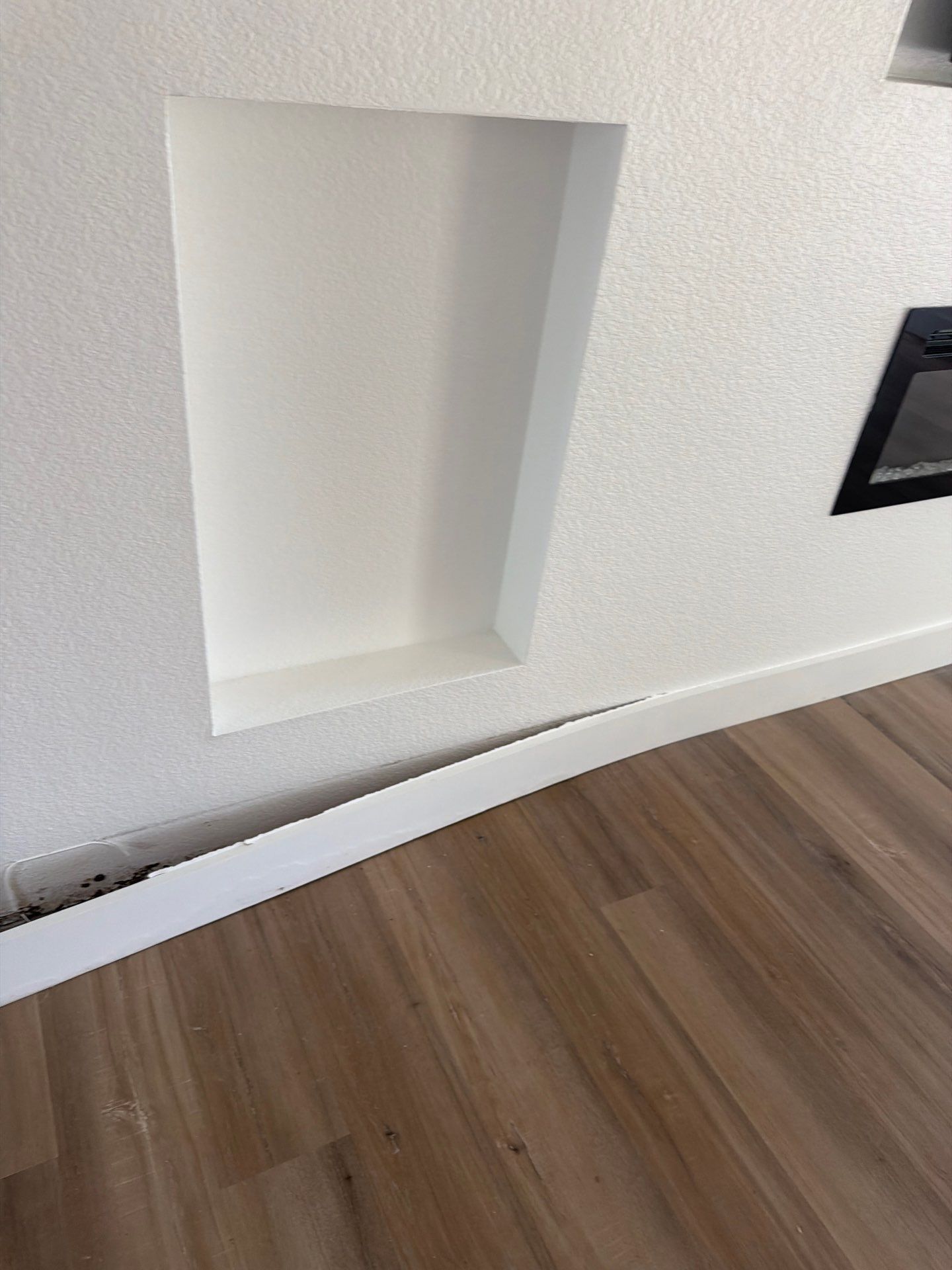 Built-in wall niche above white baseboard and wood floor in a modern interior