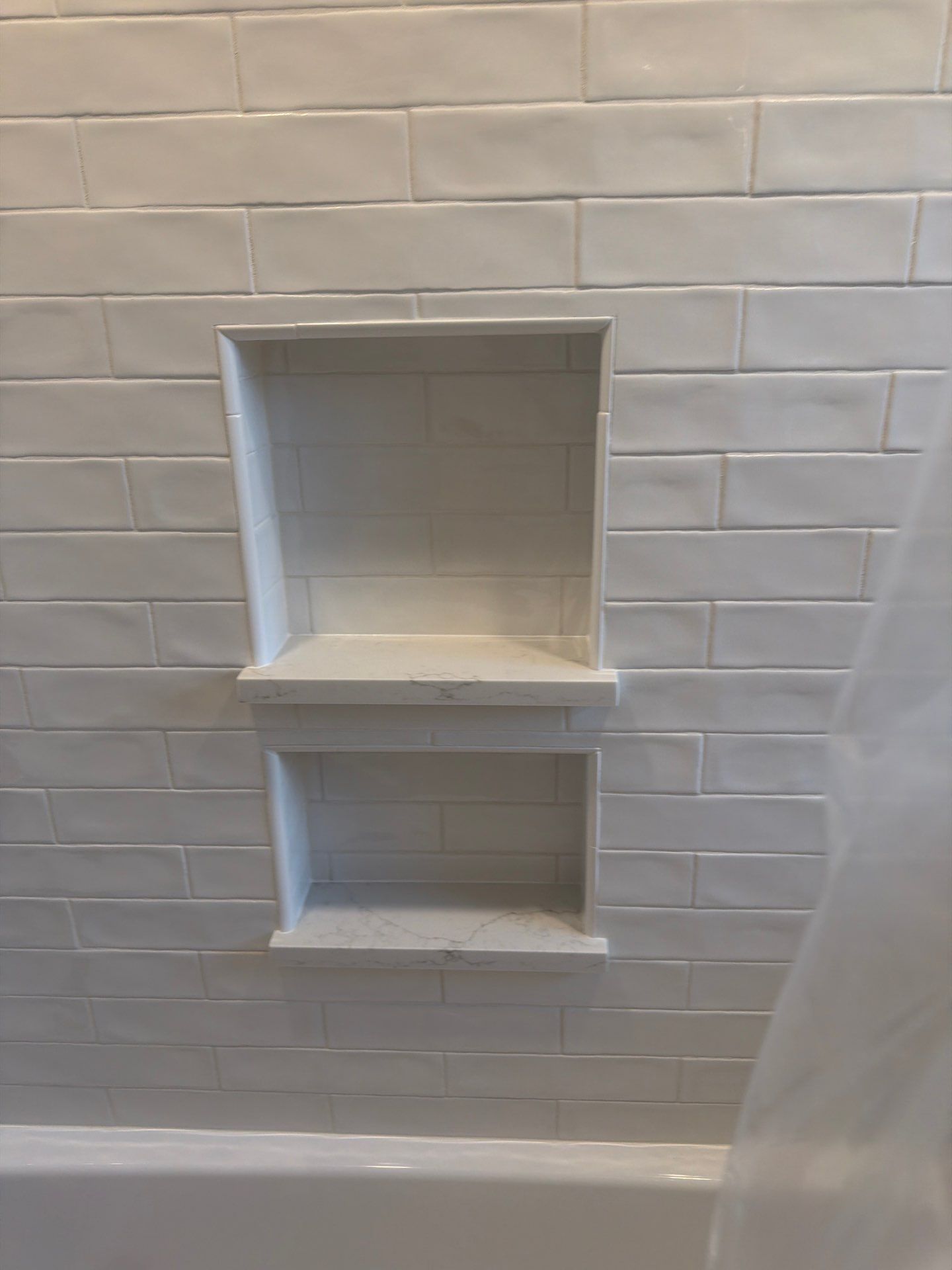 Built-in white tiled shower niche with two shelves above the bathtub