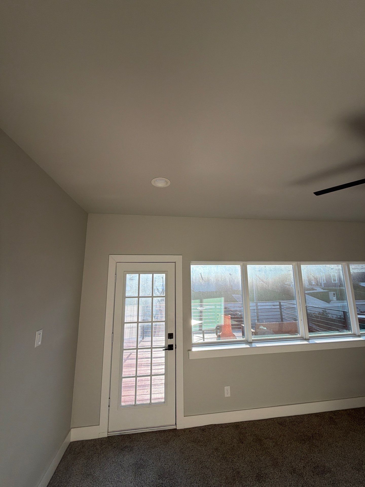 Empty room with gray walls, carpet, a glass door, and large windows letting in daylight.