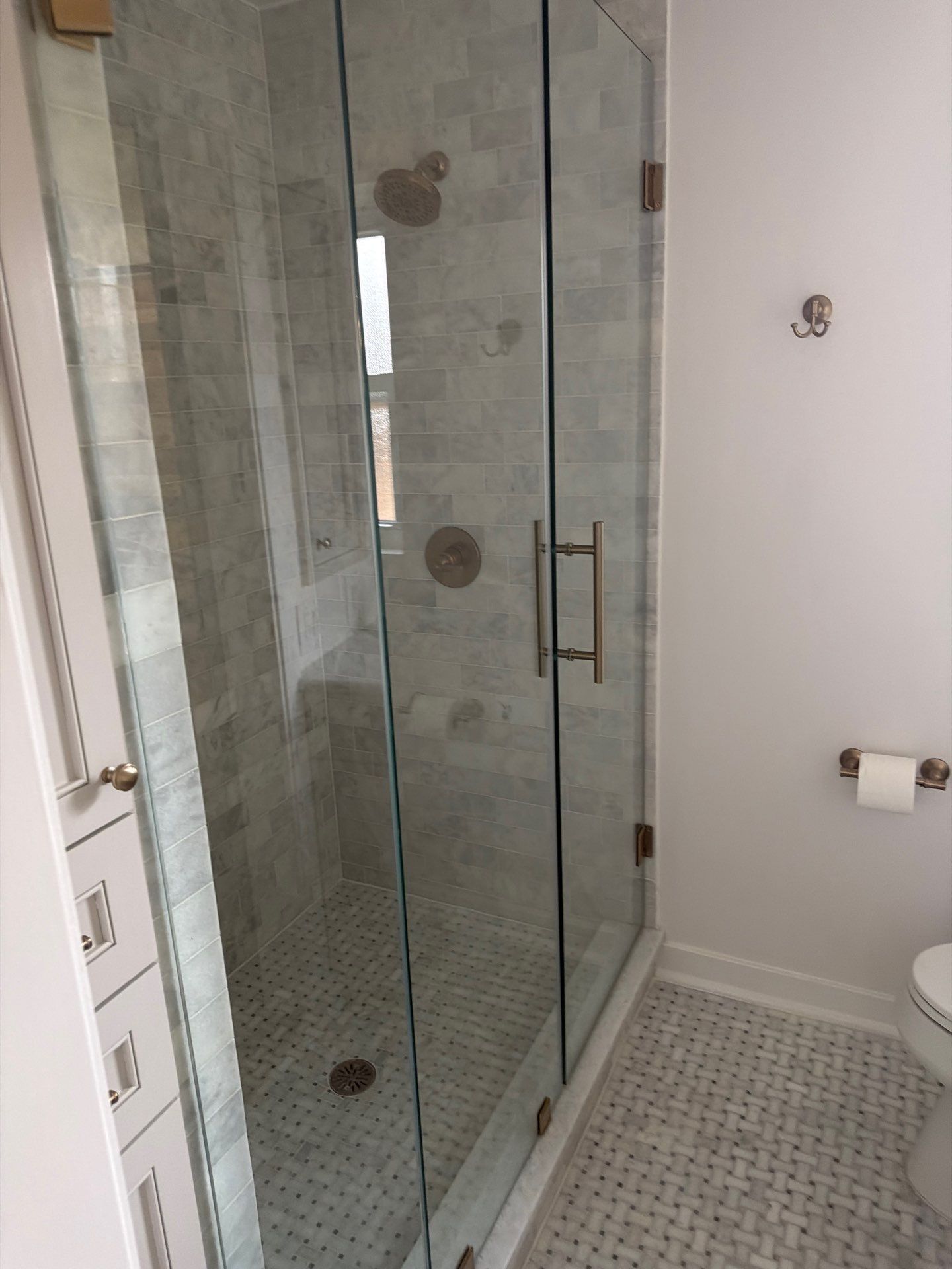 Bathroom with a glass shower door, tiled floor, and toilet paper holder on the wall