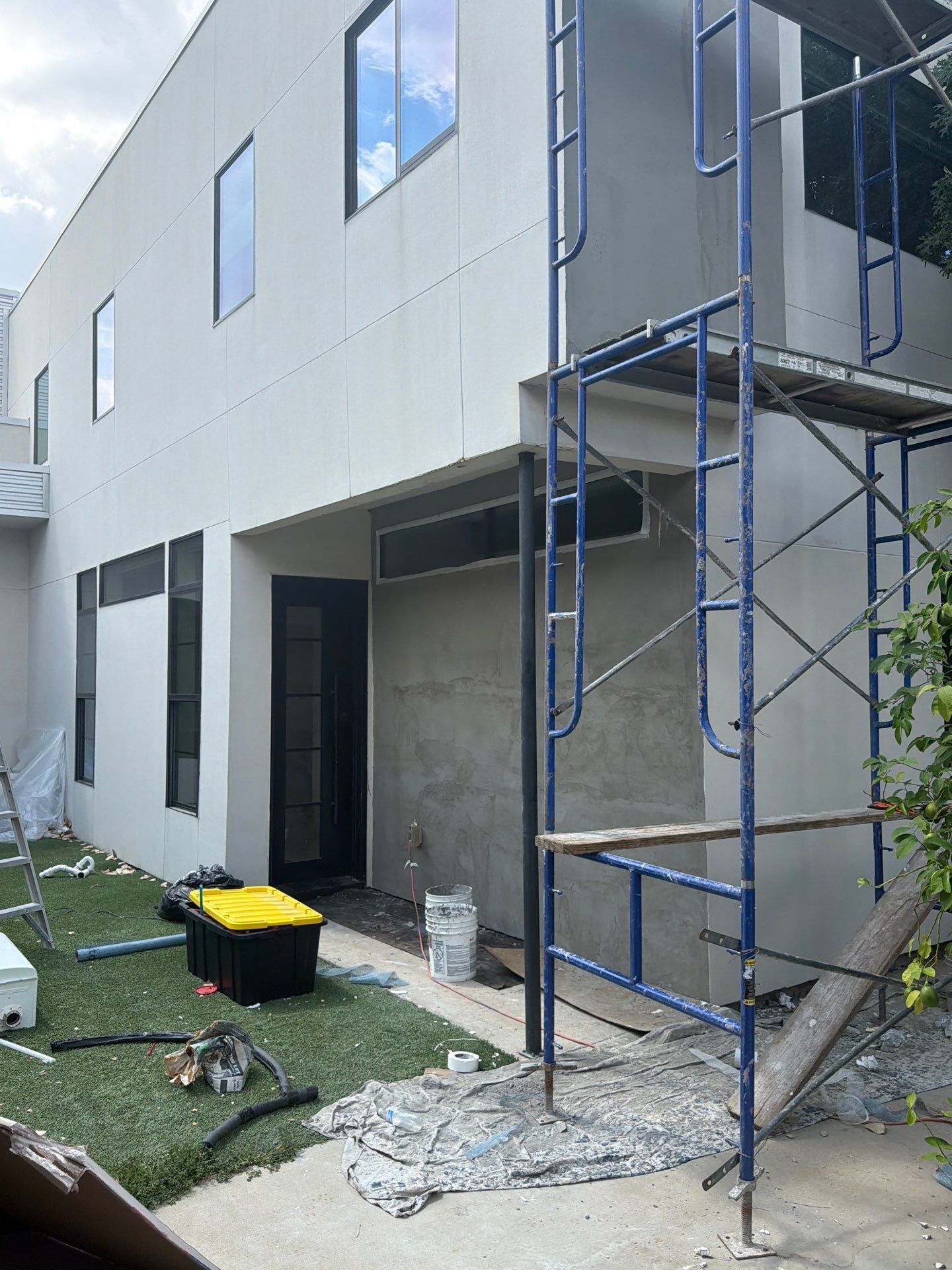 Building exterior with blue scaffolding beside an open doorway and construction materials on the ground