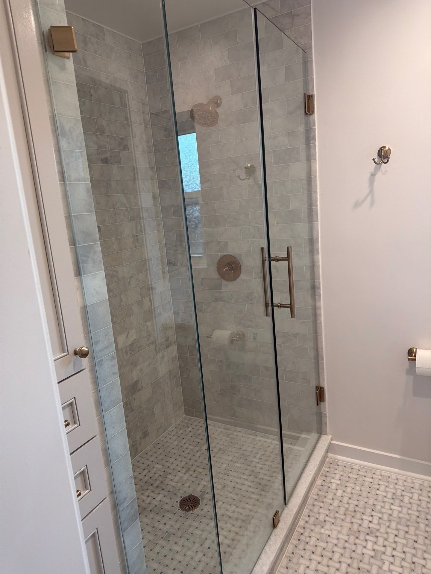 Glass shower stall with tiled floor and white bathroom walls