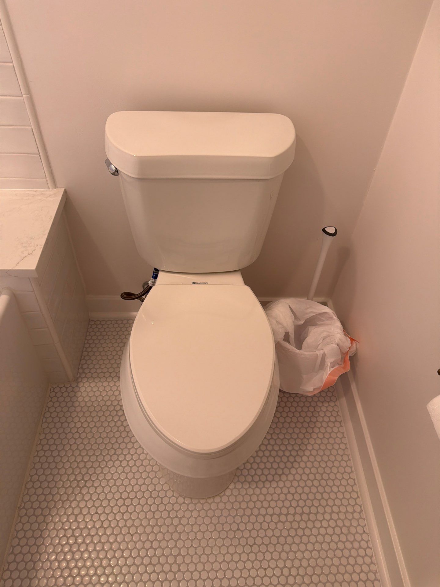 Small bathroom with a white toilet and a plastic bag on the floor beside it.