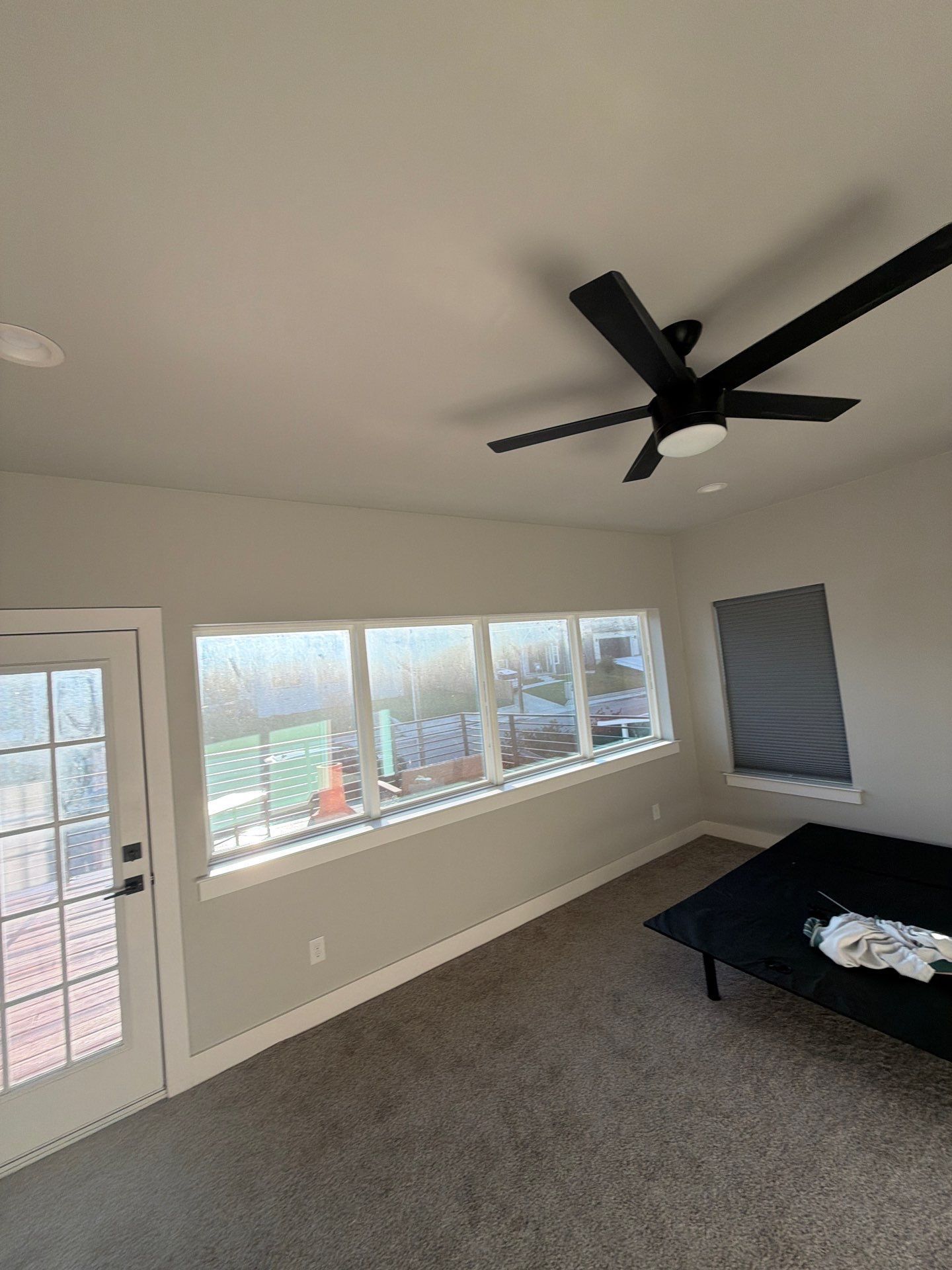 Empty beige room with carpet, ceiling fan, windows, and a door