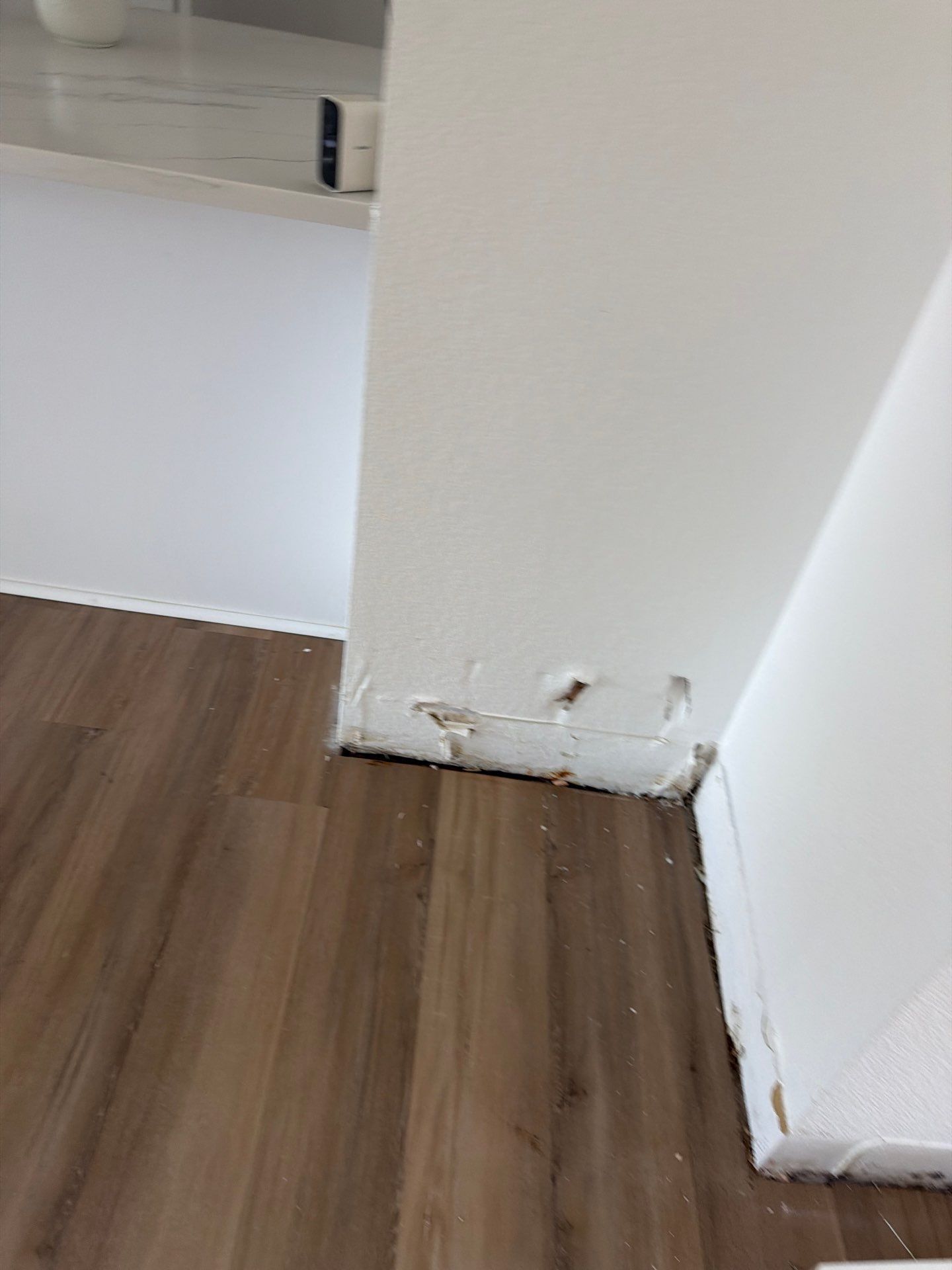 Damaged white wall corner with peeling paint above a wood floor in an empty room