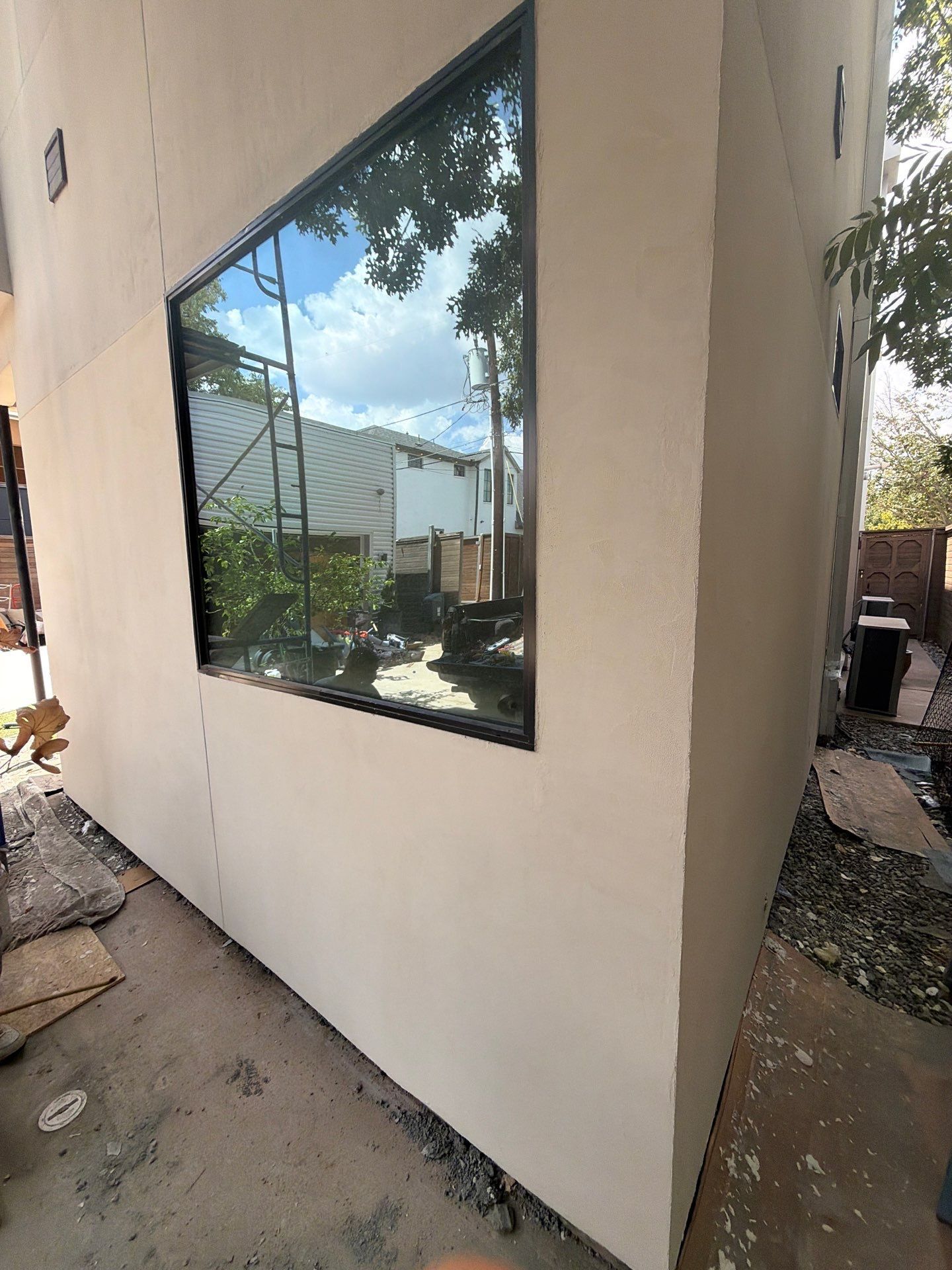 White stucco building corner with a large reflective window and a narrow side walkway outdoors