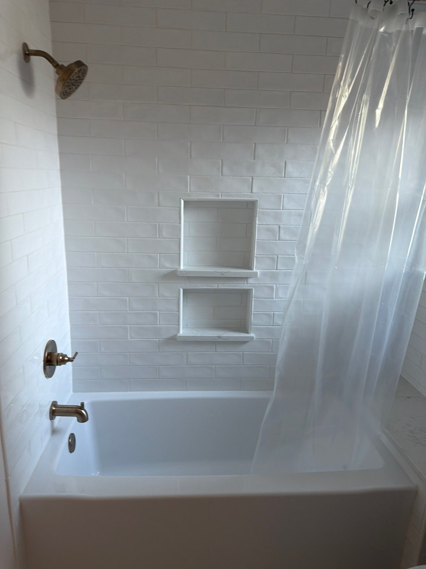 White tiled bathroom with a bathtub, shower curtain, and built-in wall shelves under the showerhead