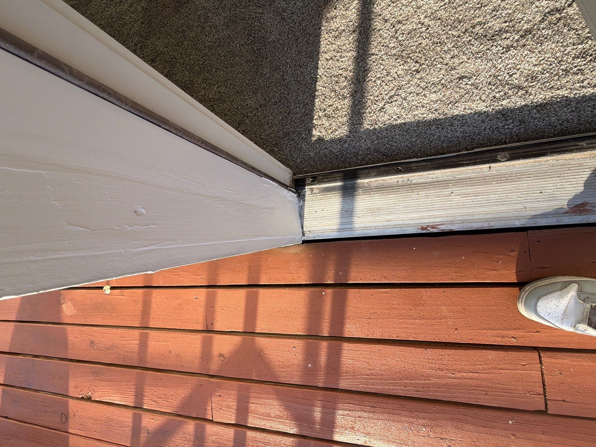 White siding and red brick patio beside a shadowed concrete step and a white sneaker at the edge.