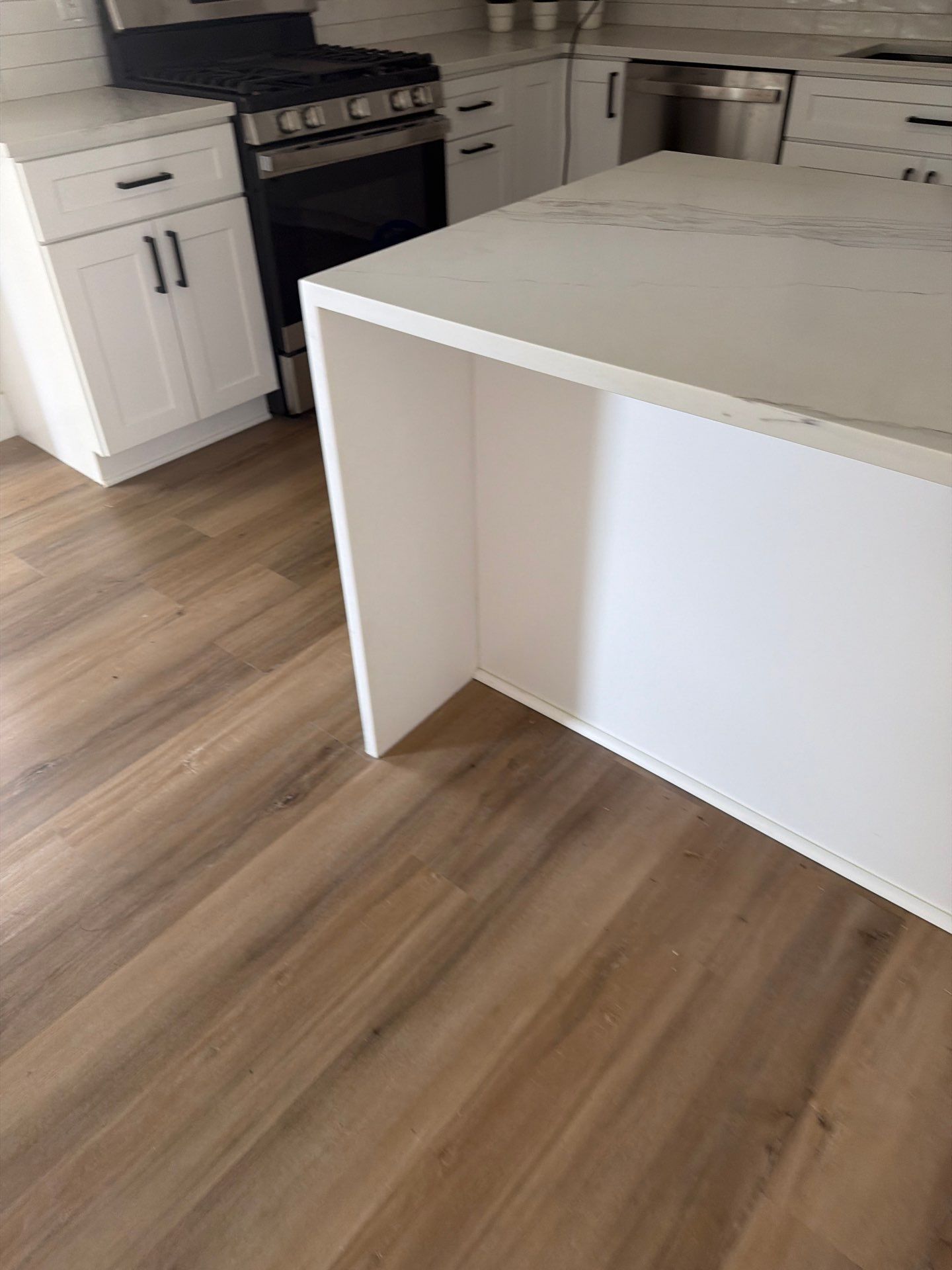 Modern kitchen with white cabinets, black stove, wood floors, and a white island in the foreground