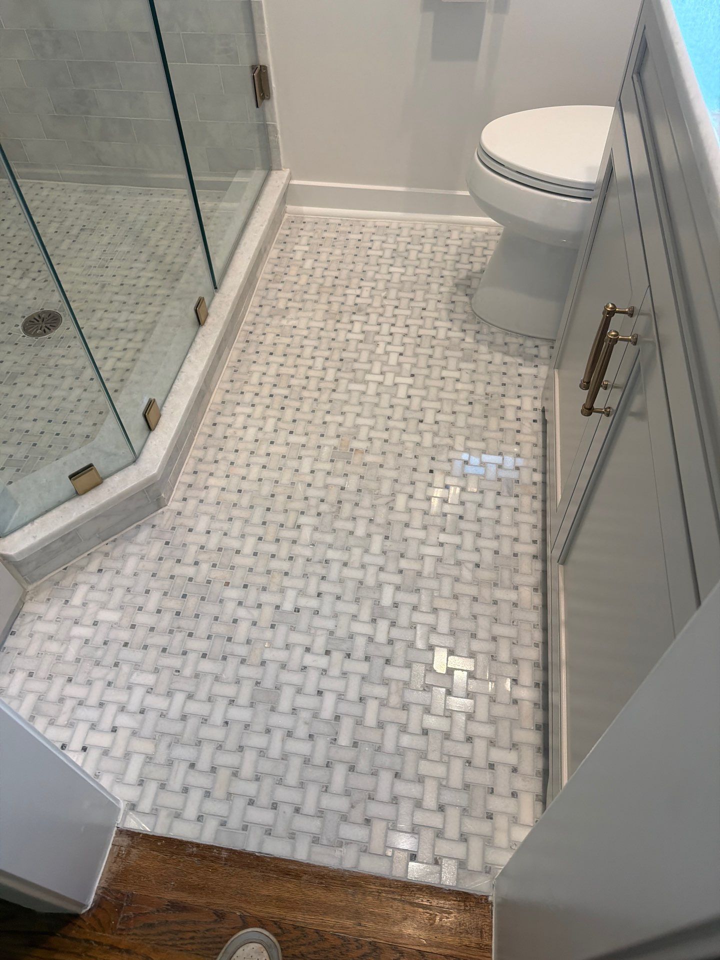 Small bathroom with glass shower, mosaic tile floor, and toilet visible in the corner.