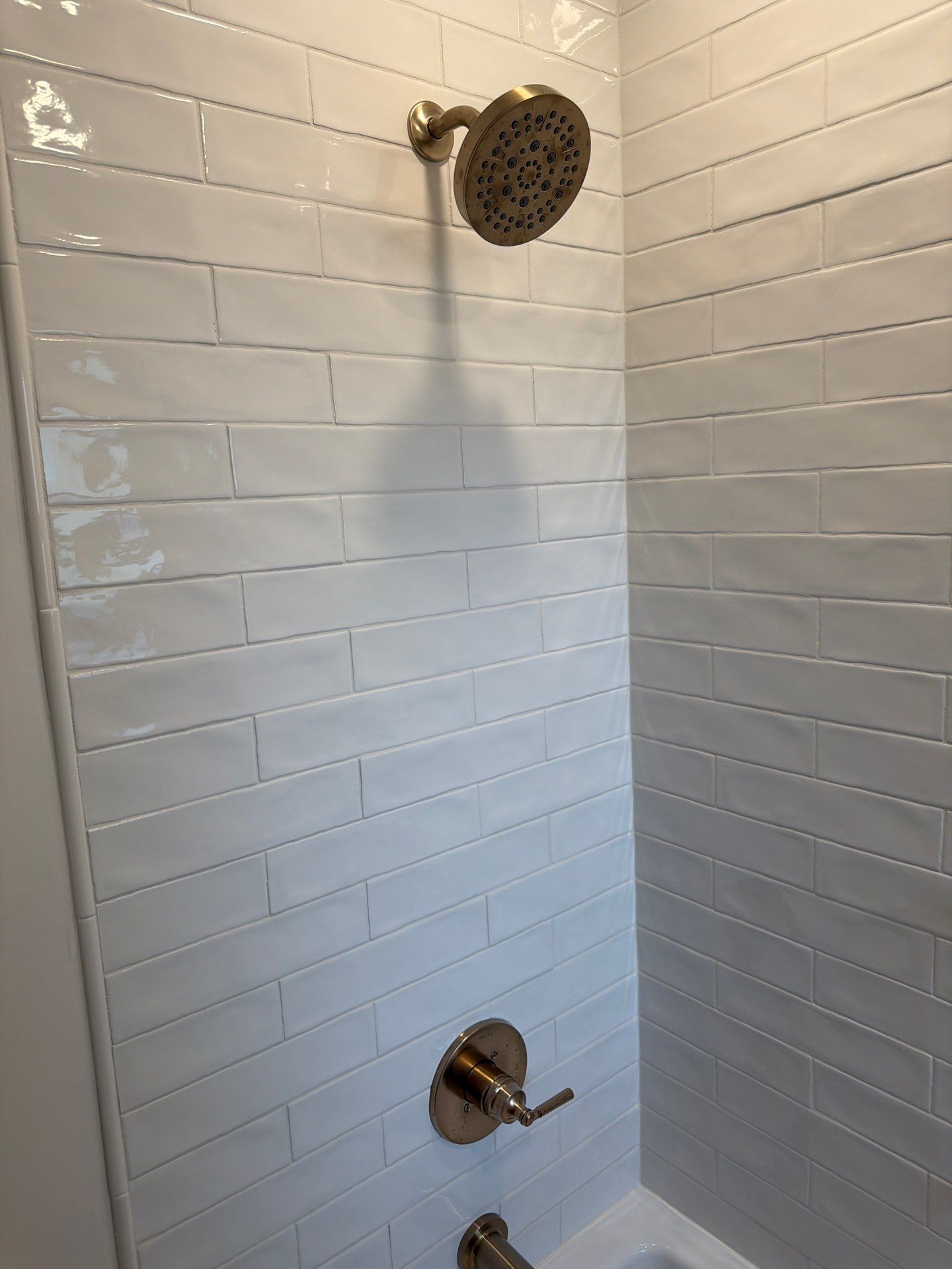 White tiled shower with bronze showerhead and tub spout in a bathroom corner.