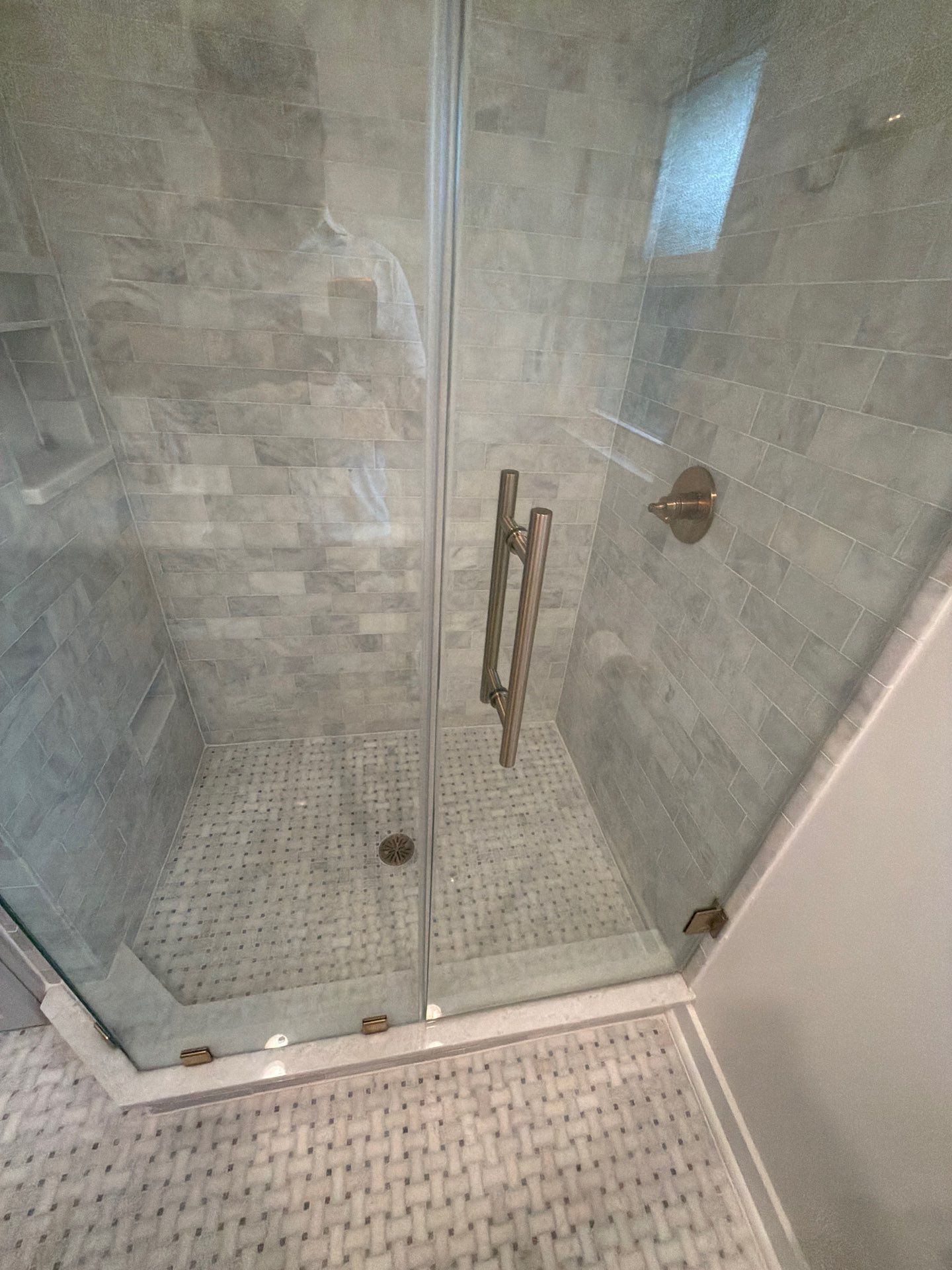 Glass walk-in shower with tiled floor and gray stone walls, viewed from outside the bathroom doorway