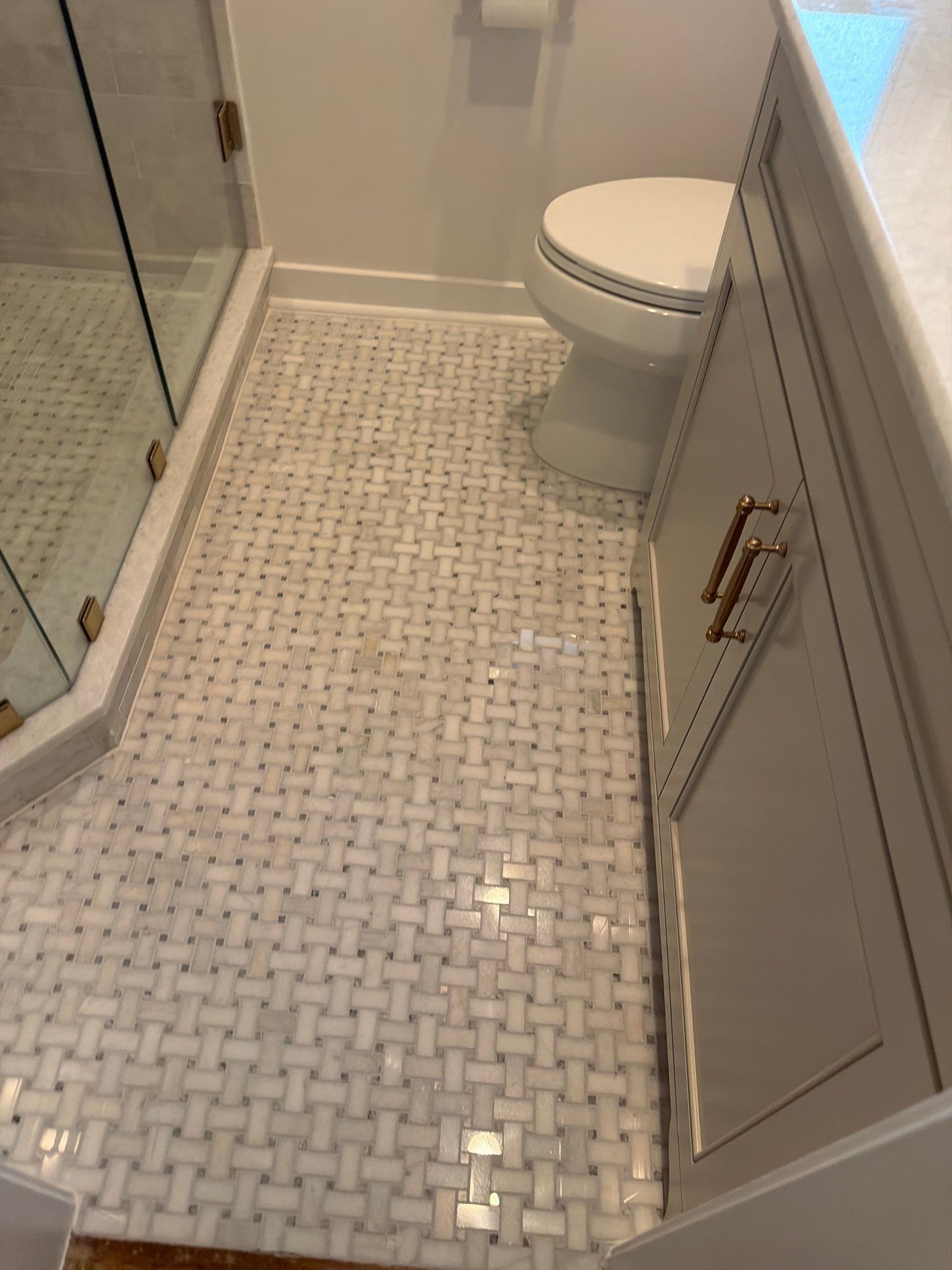 Narrow bathroom with white mosaic tile floor, glass shower on left, toilet ahead, and cabinet on right