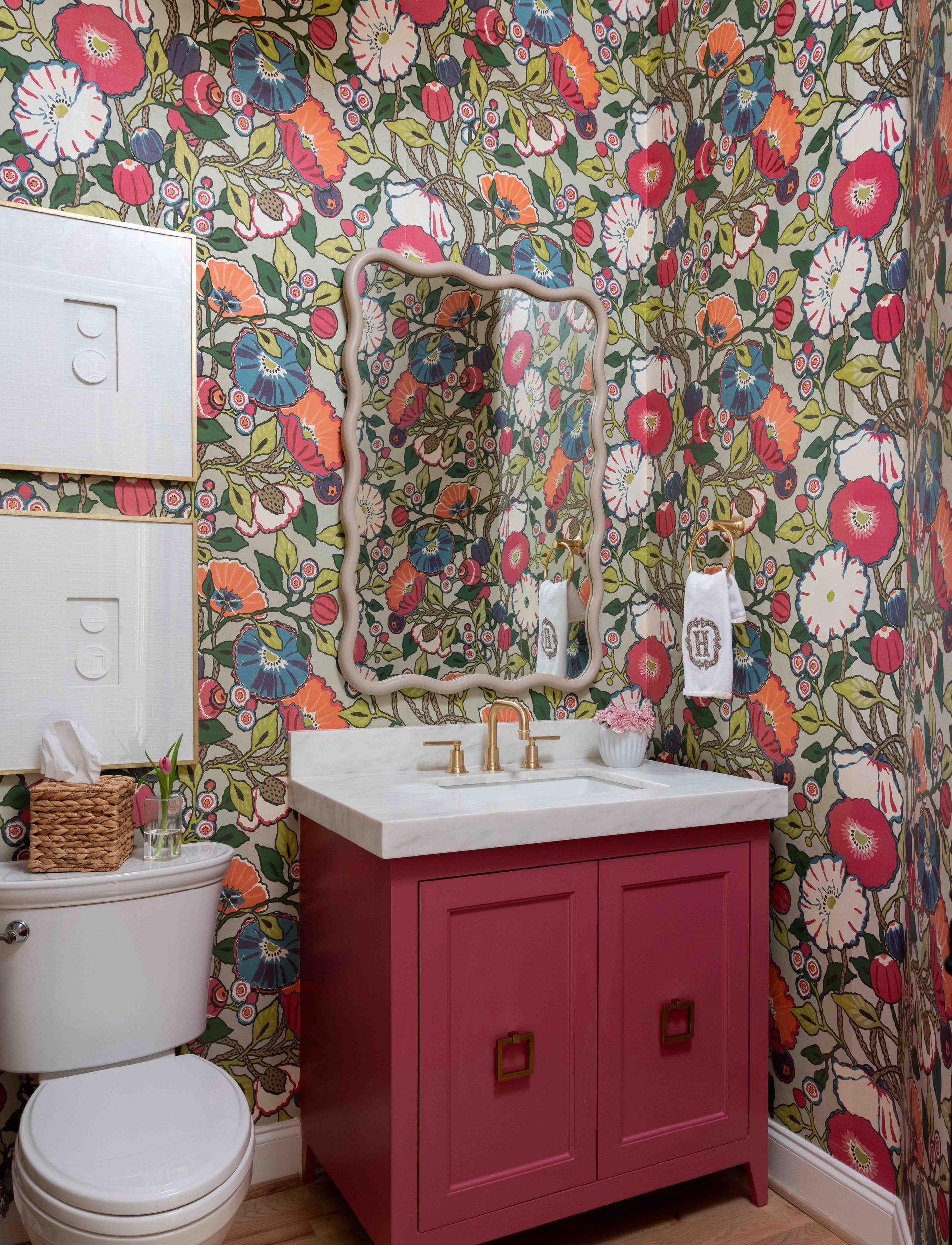 Floral wallpaper bathroom with a pink vanity, white sink, mirror, and toilet.
