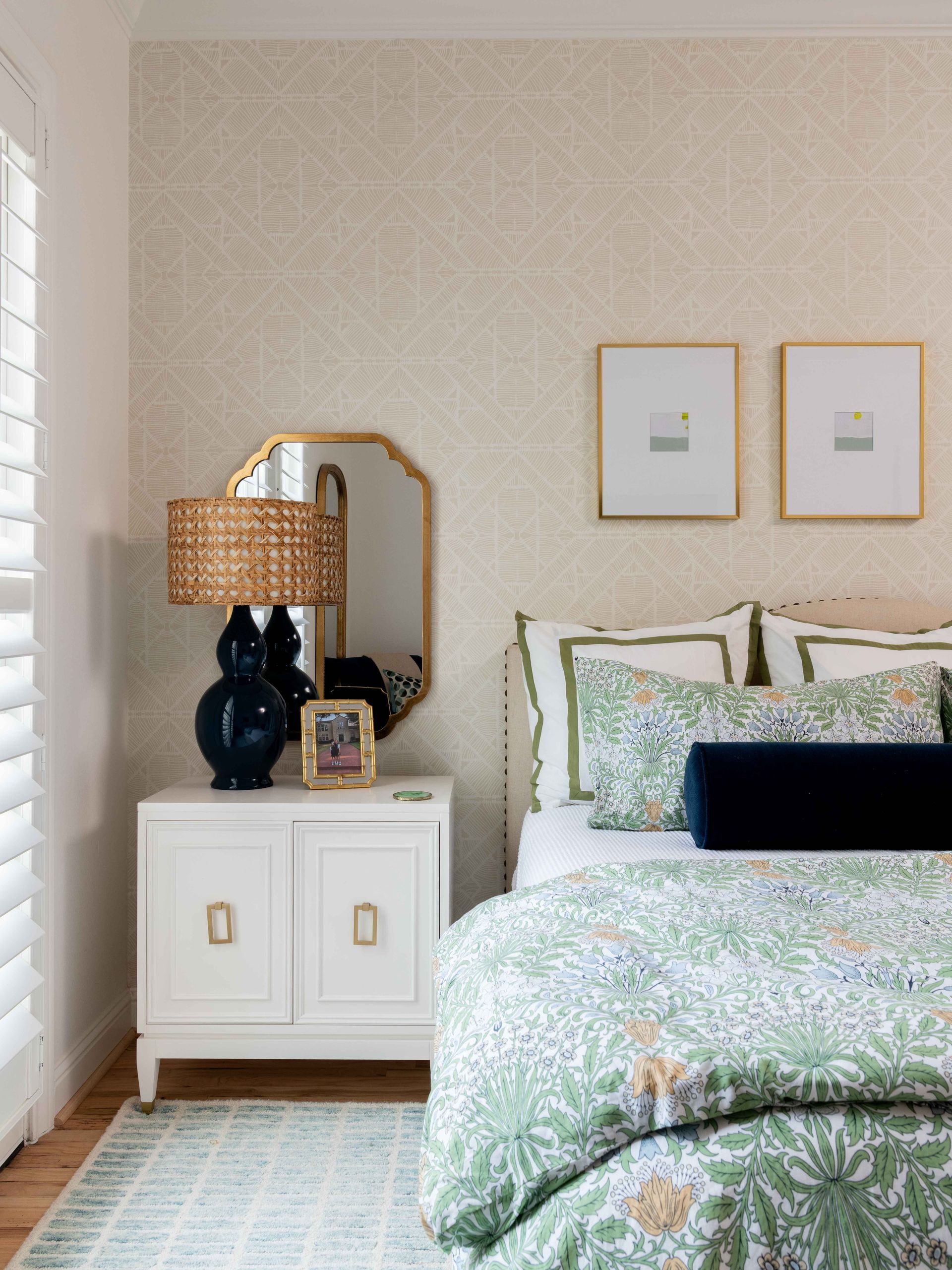Cozy bedroom with a bed, patterned green bedding, white nightstand, lamp, and wall art.