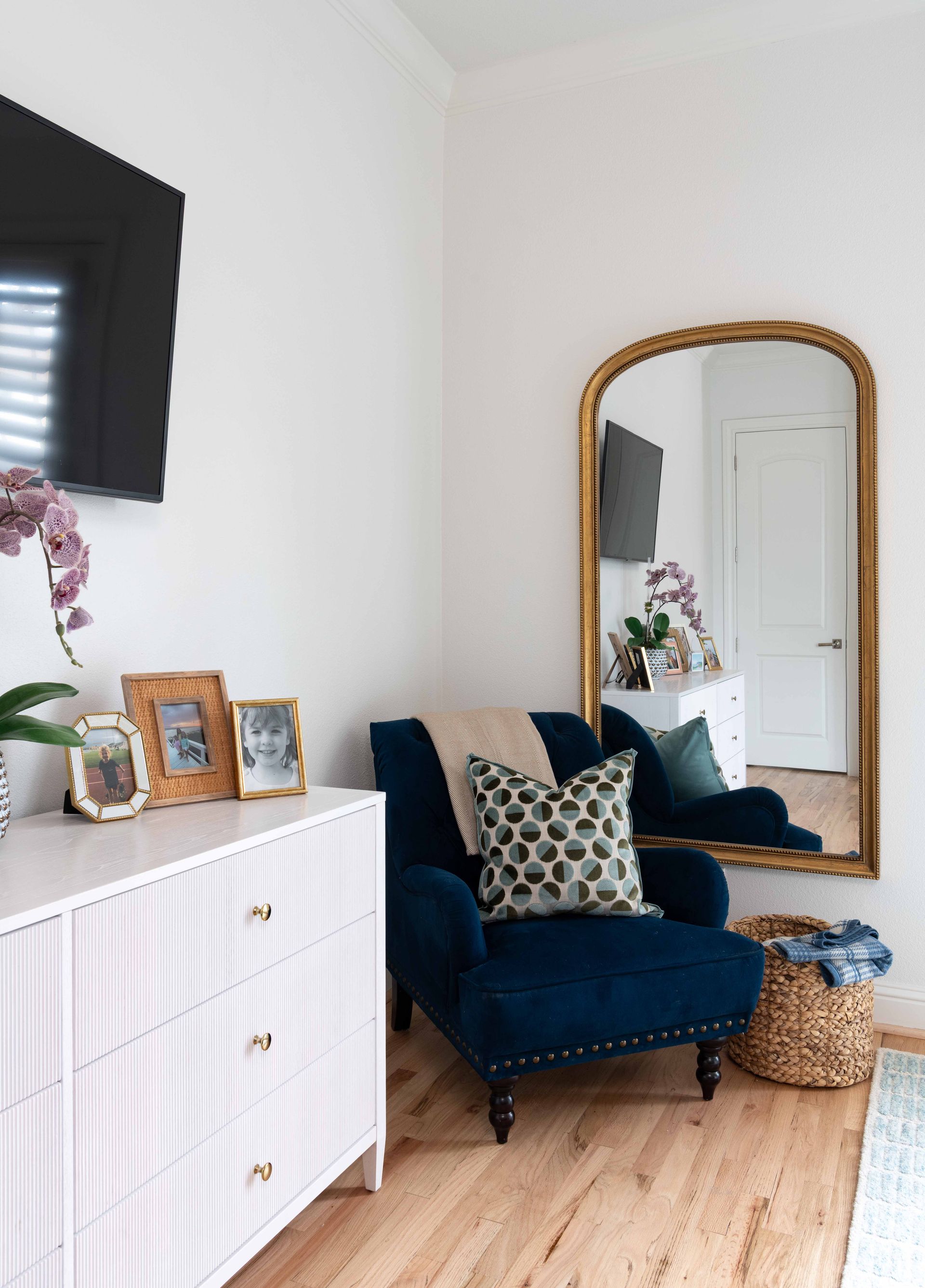 Cozy corner with navy chair, gold-framed mirror, white cabinet, and woven basket in a bright room