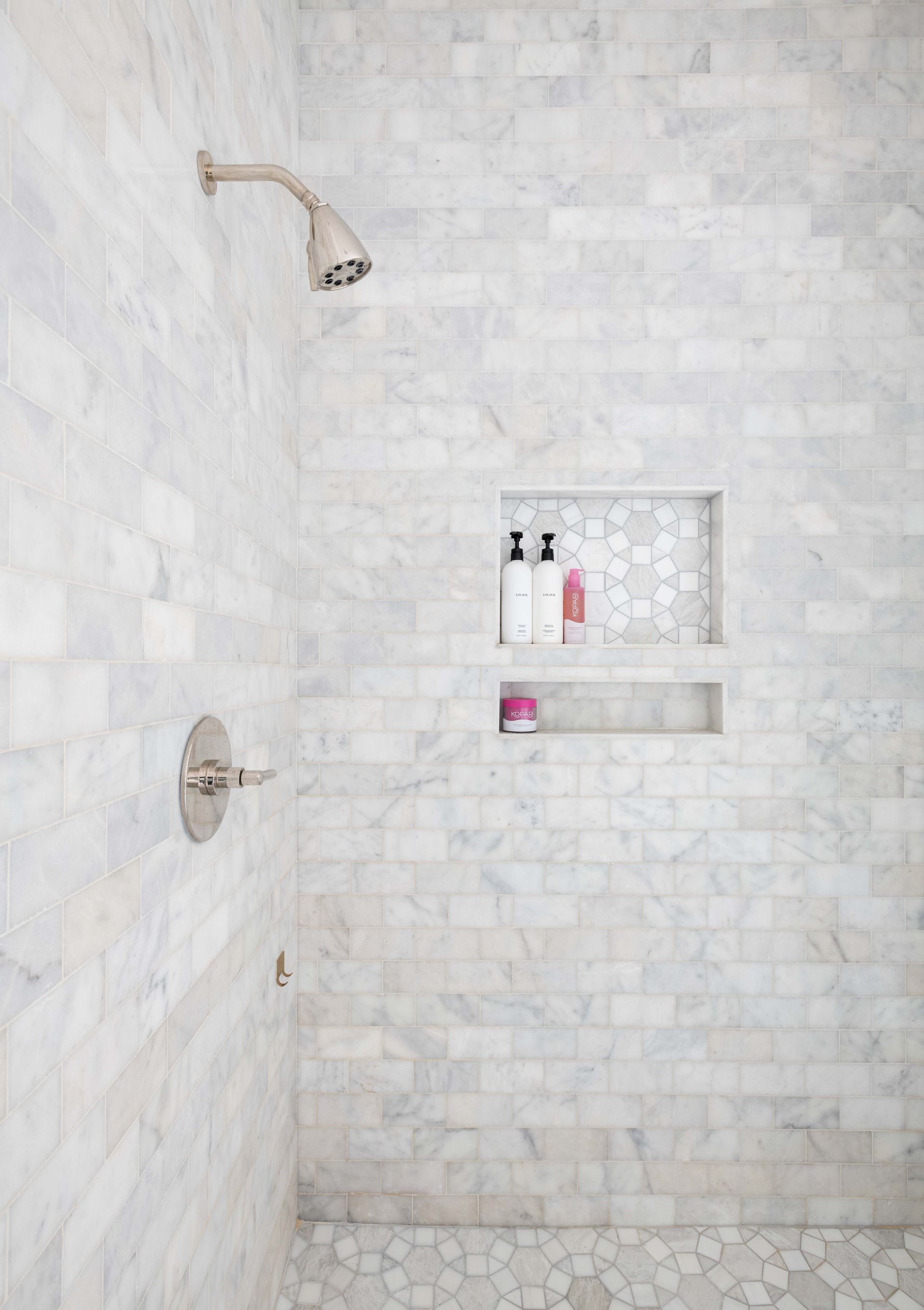 White tiled shower with chrome fixtures and two built-in shelves holding toiletries.