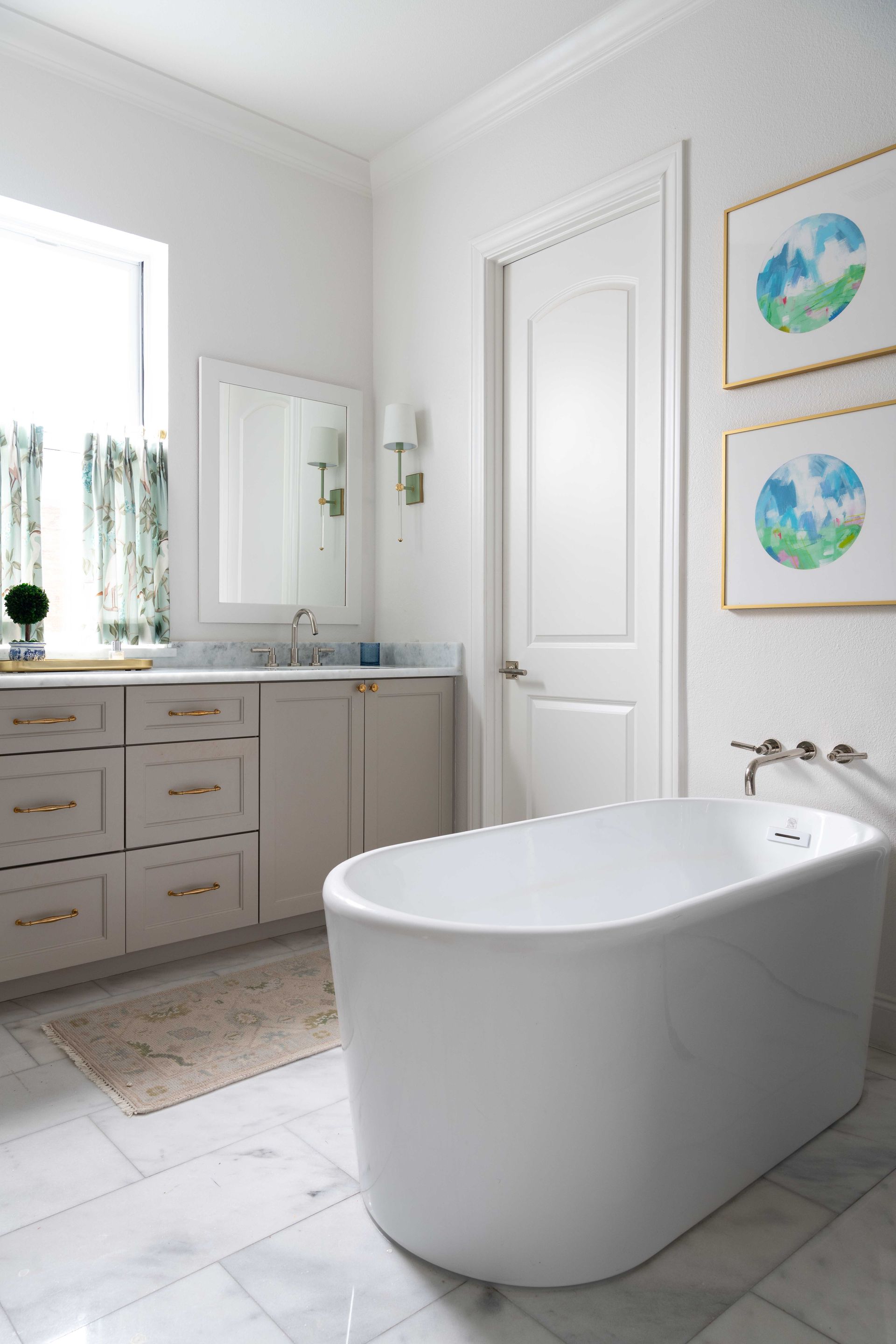 Bright white bathroom with a freestanding tub, vanity, mirror, and framed art.