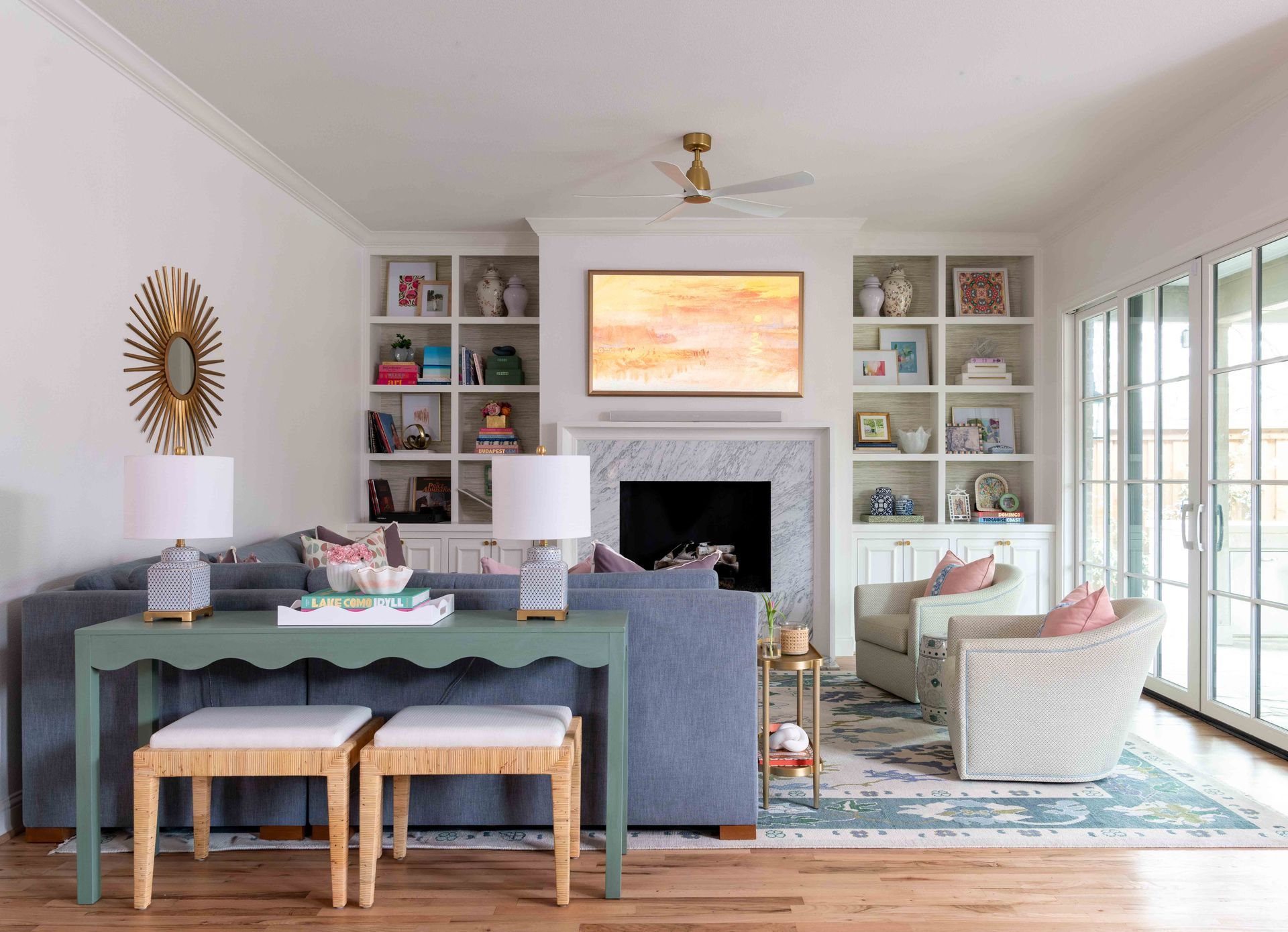 Bright living room with built-in shelves, fireplace, teal dining table, and white armchair by windows