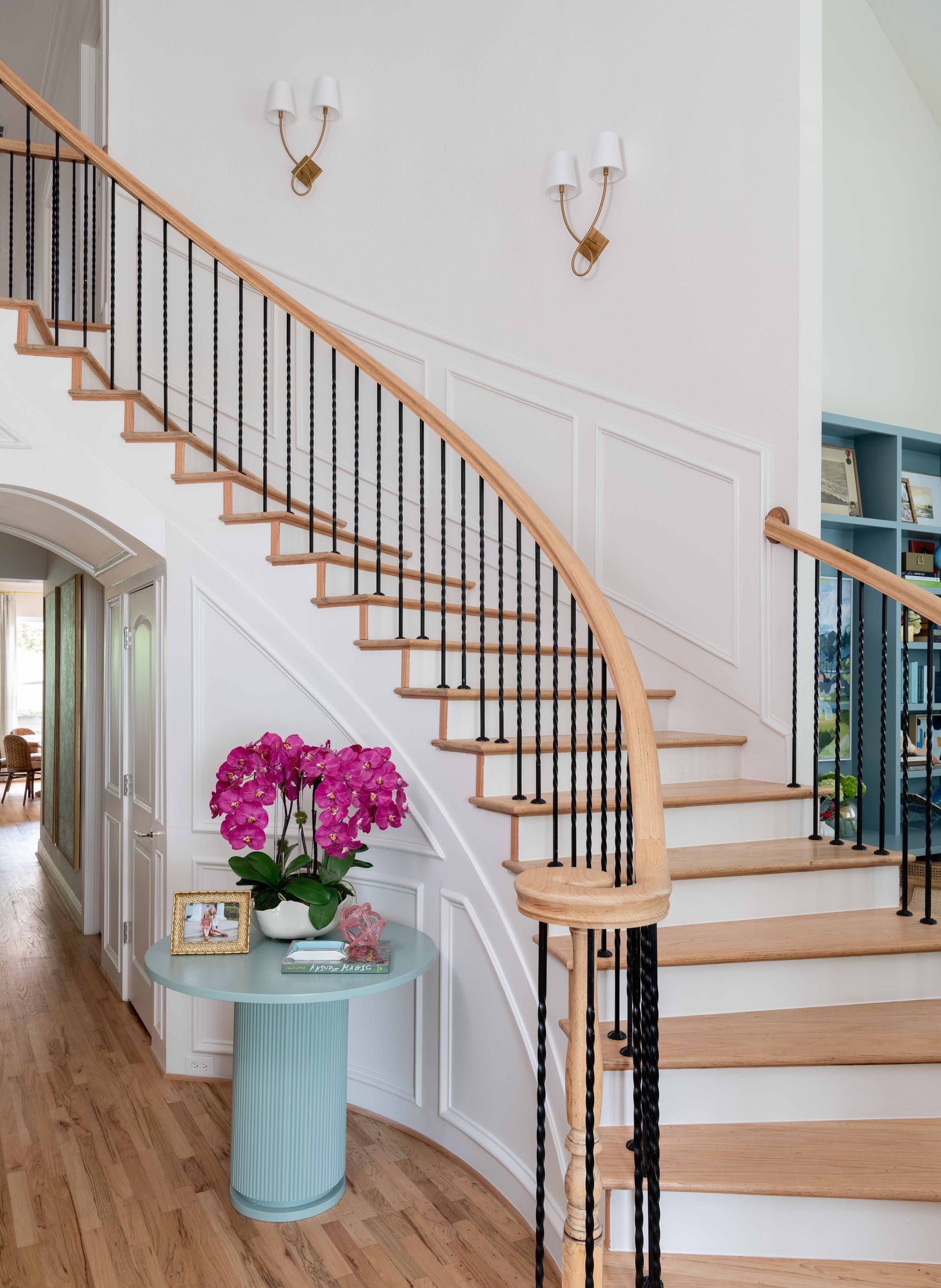 Elegant curved staircase in a bright foyer beside a small round table with pink flowers