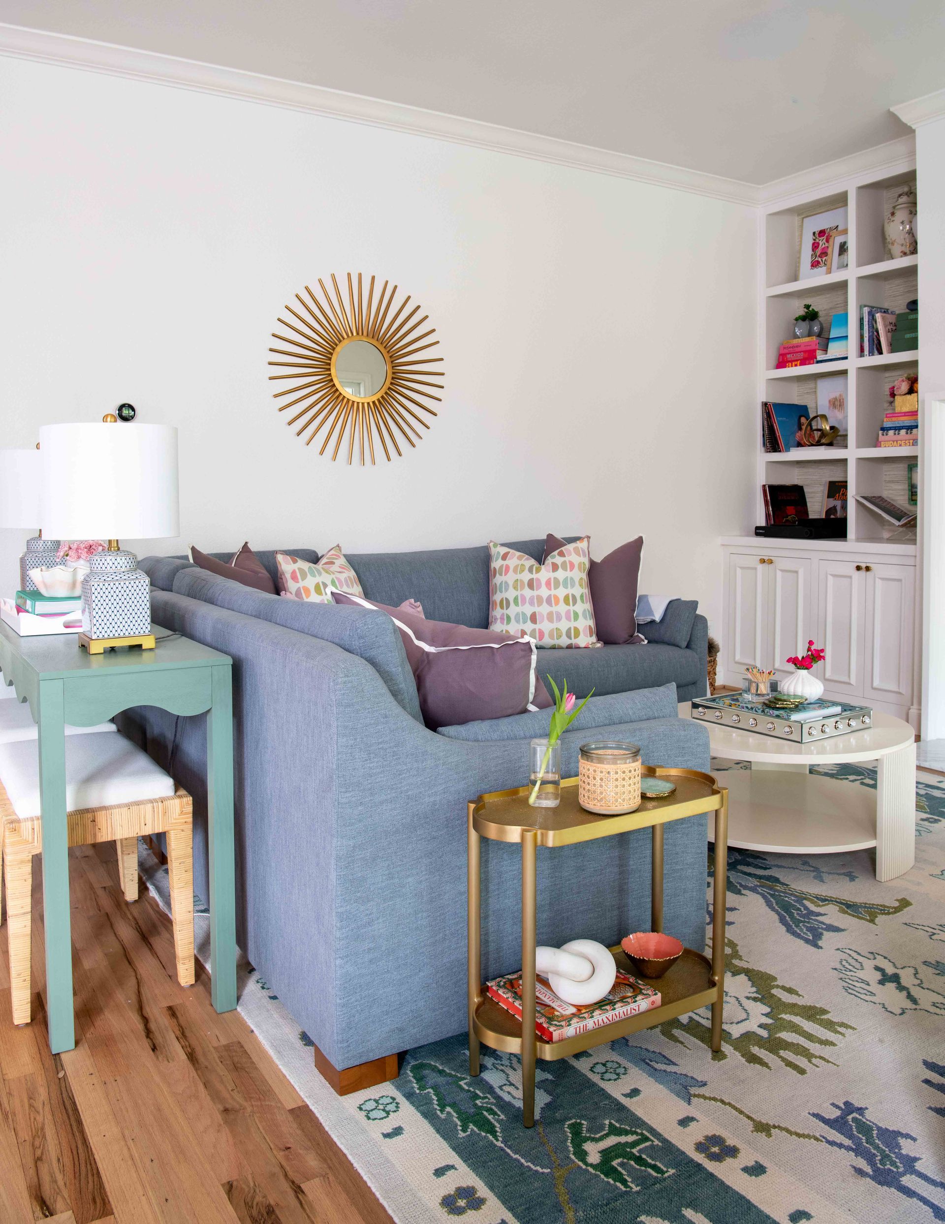 Bright living room with blue sofa, white shelves, teal table, gold decor, and patterned rug.