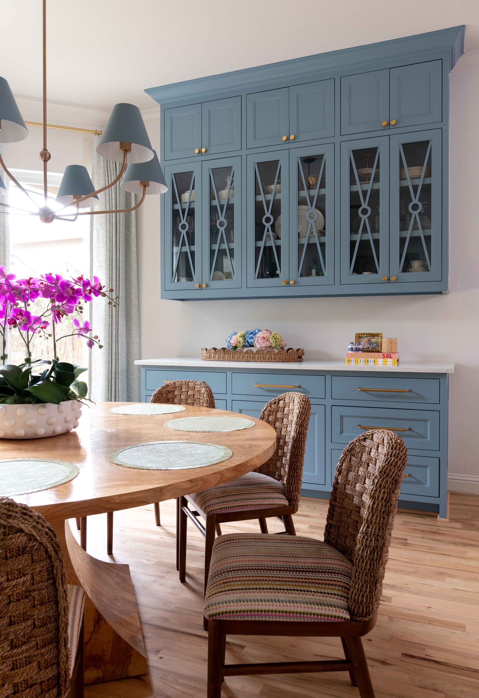 Light blue china cabinet and buffet in a bright dining room with wicker chairs and a round wooden table