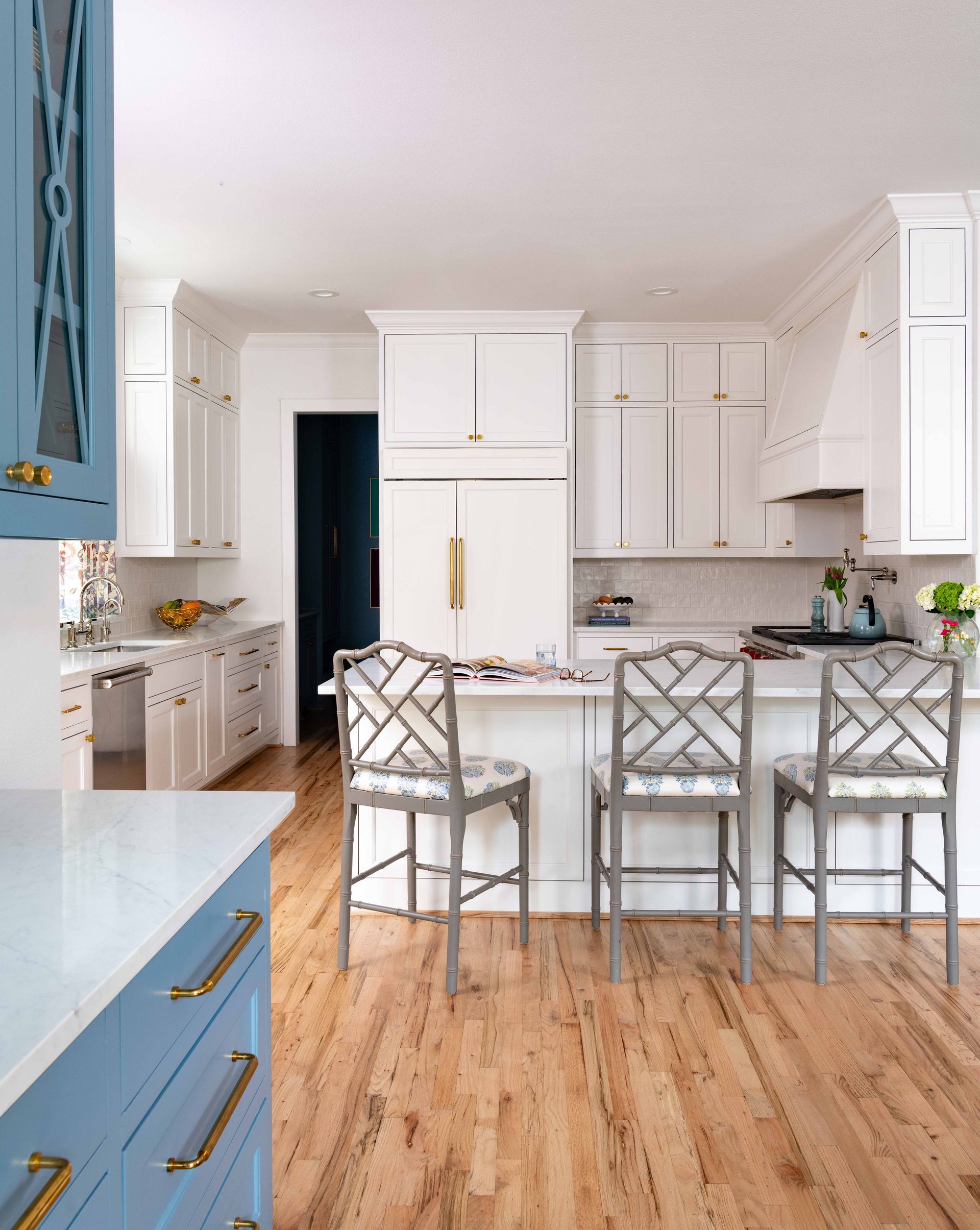 Bright white kitchen with wood floor, marble island, and three upholstered bar stools