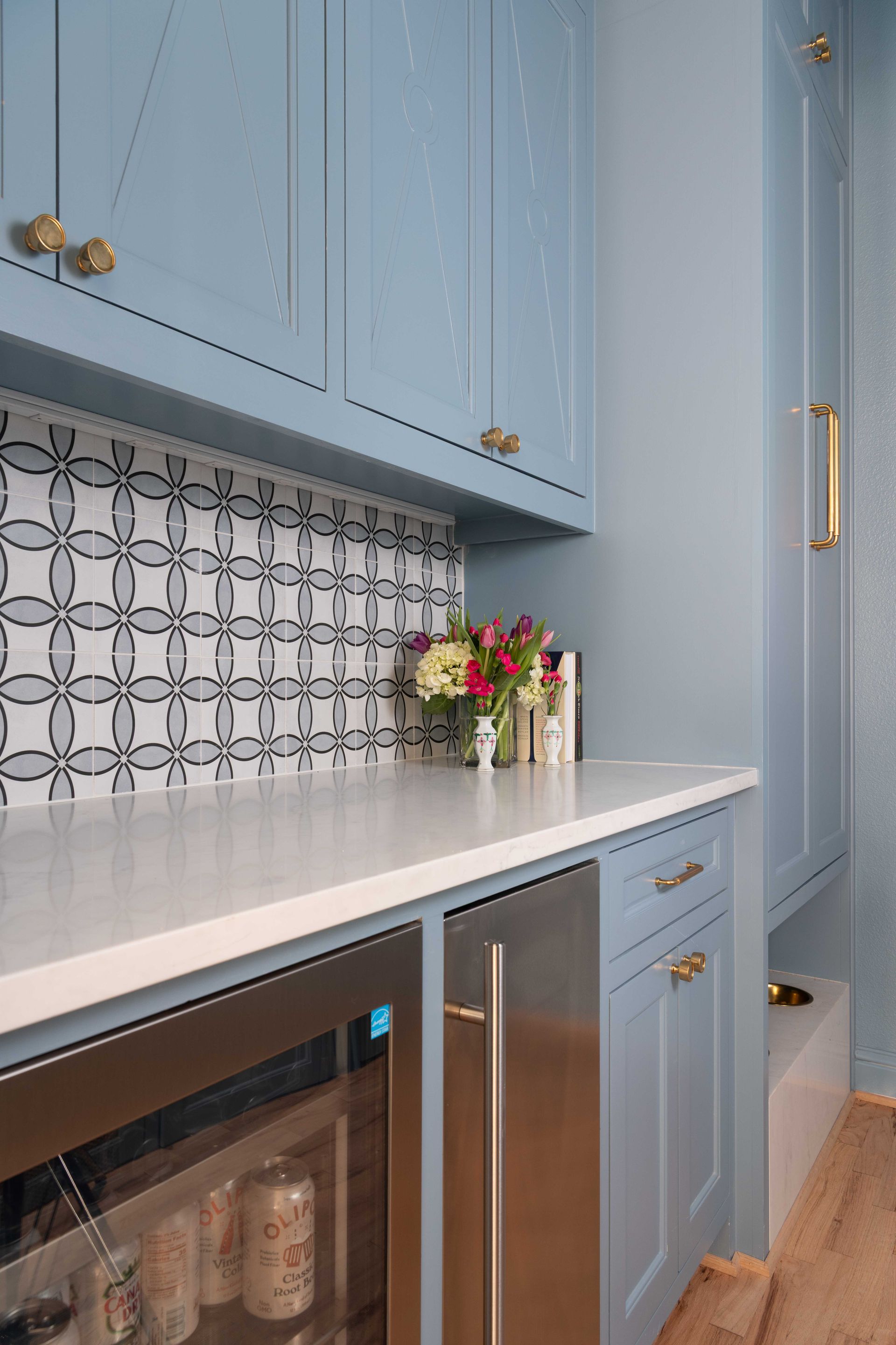 Blue kitchen cabinets and white countertop with patterned backsplash and flowers on the counter