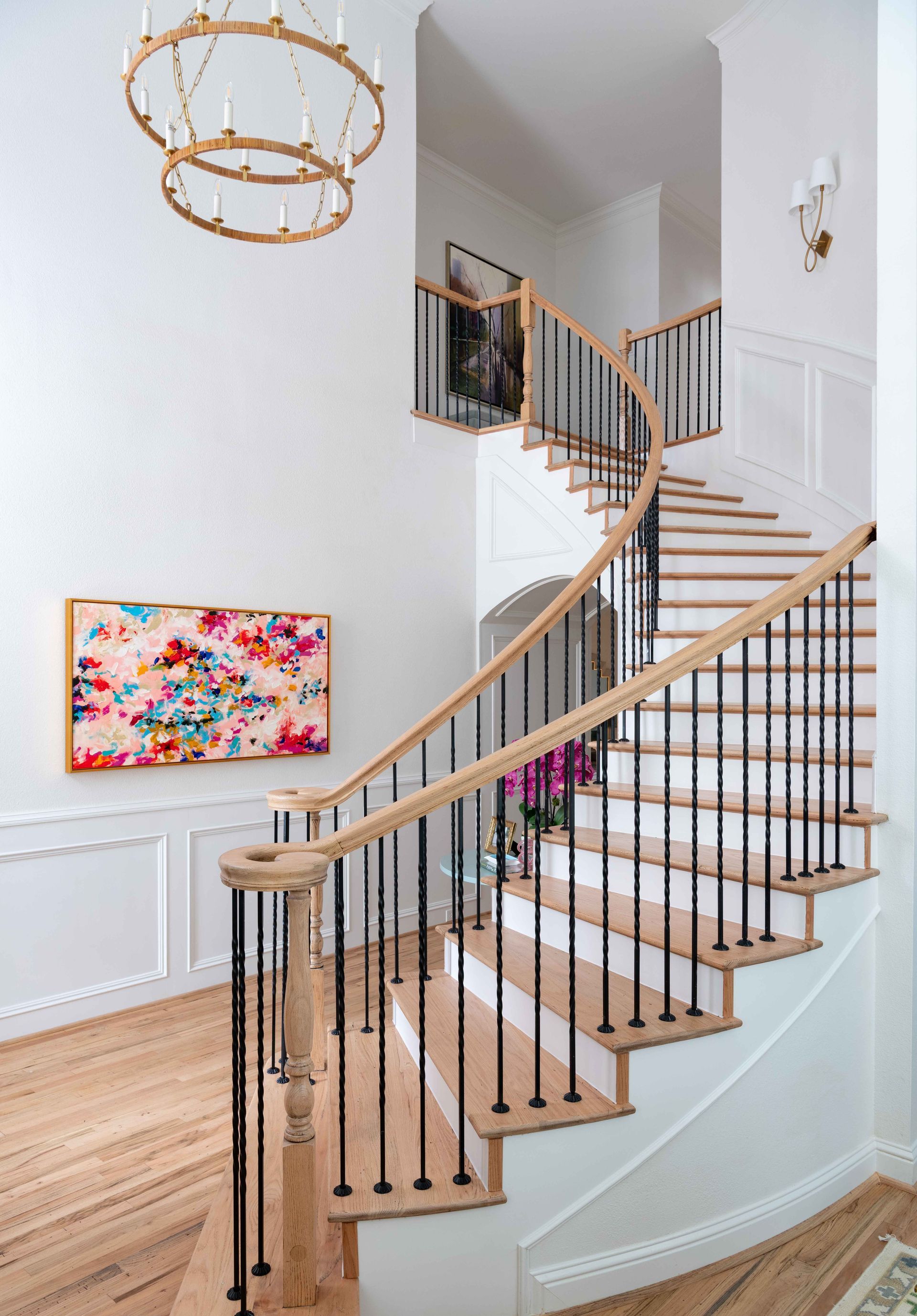 Curved staircase with wood treads and black railings in a bright modern foyer, with white walls and artwork.