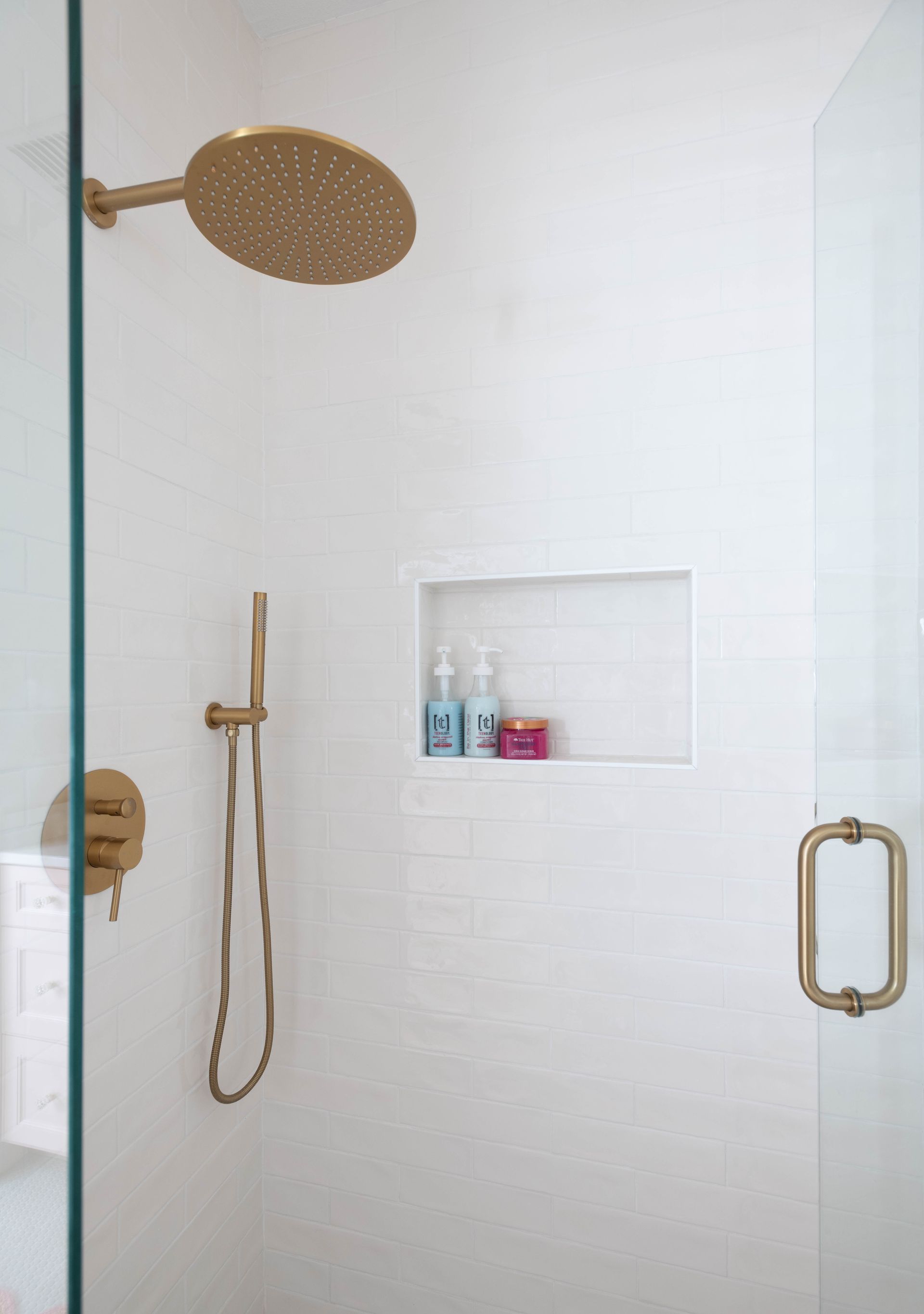 White tiled shower with gold fixtures and a built-in shelf holding toiletries