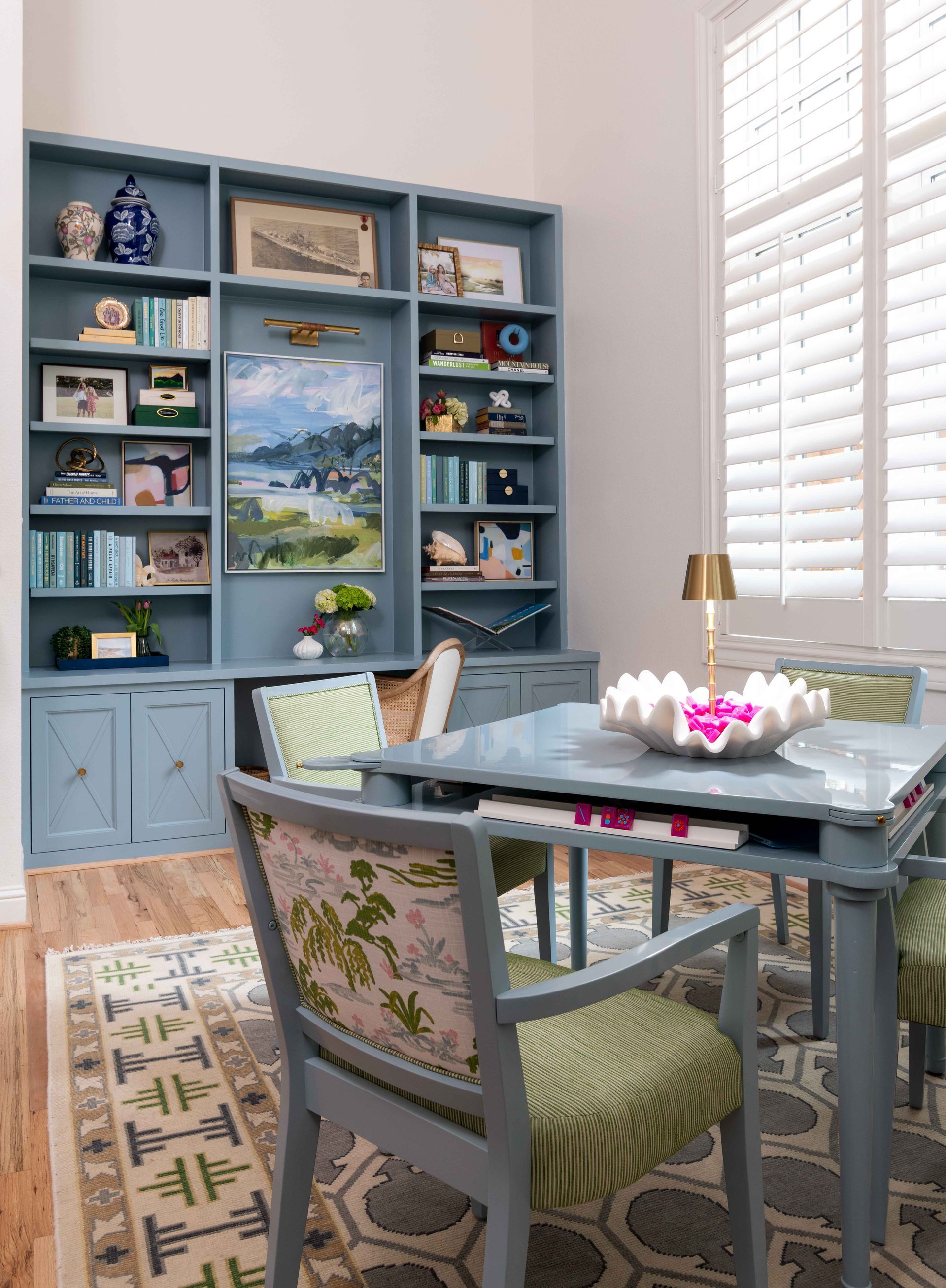 Blue home office with built-in shelves, desk, chair, and bright window shutters