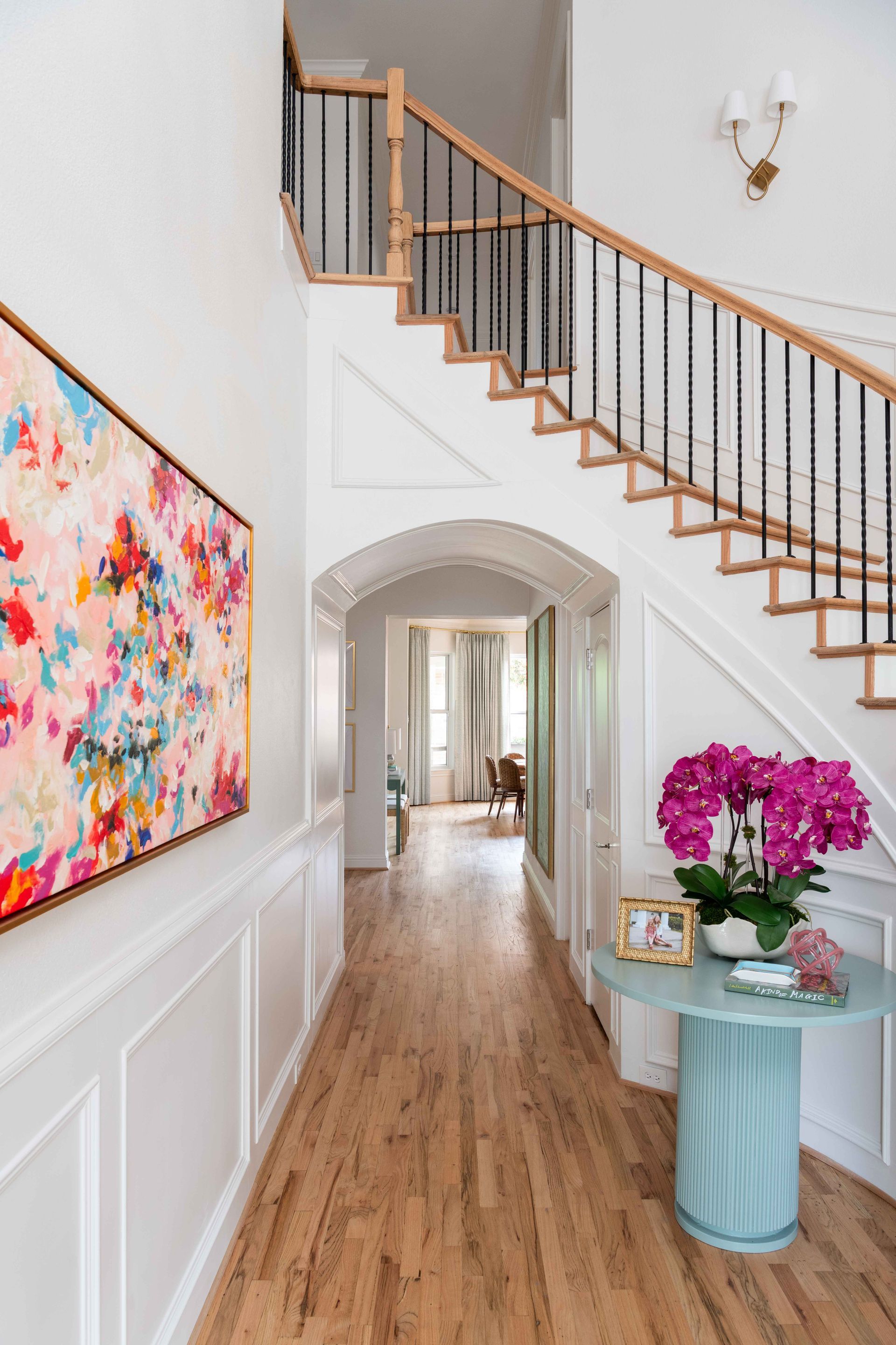 Bright hallway with staircase, colorful wall art, and a blue side table with pink flowers