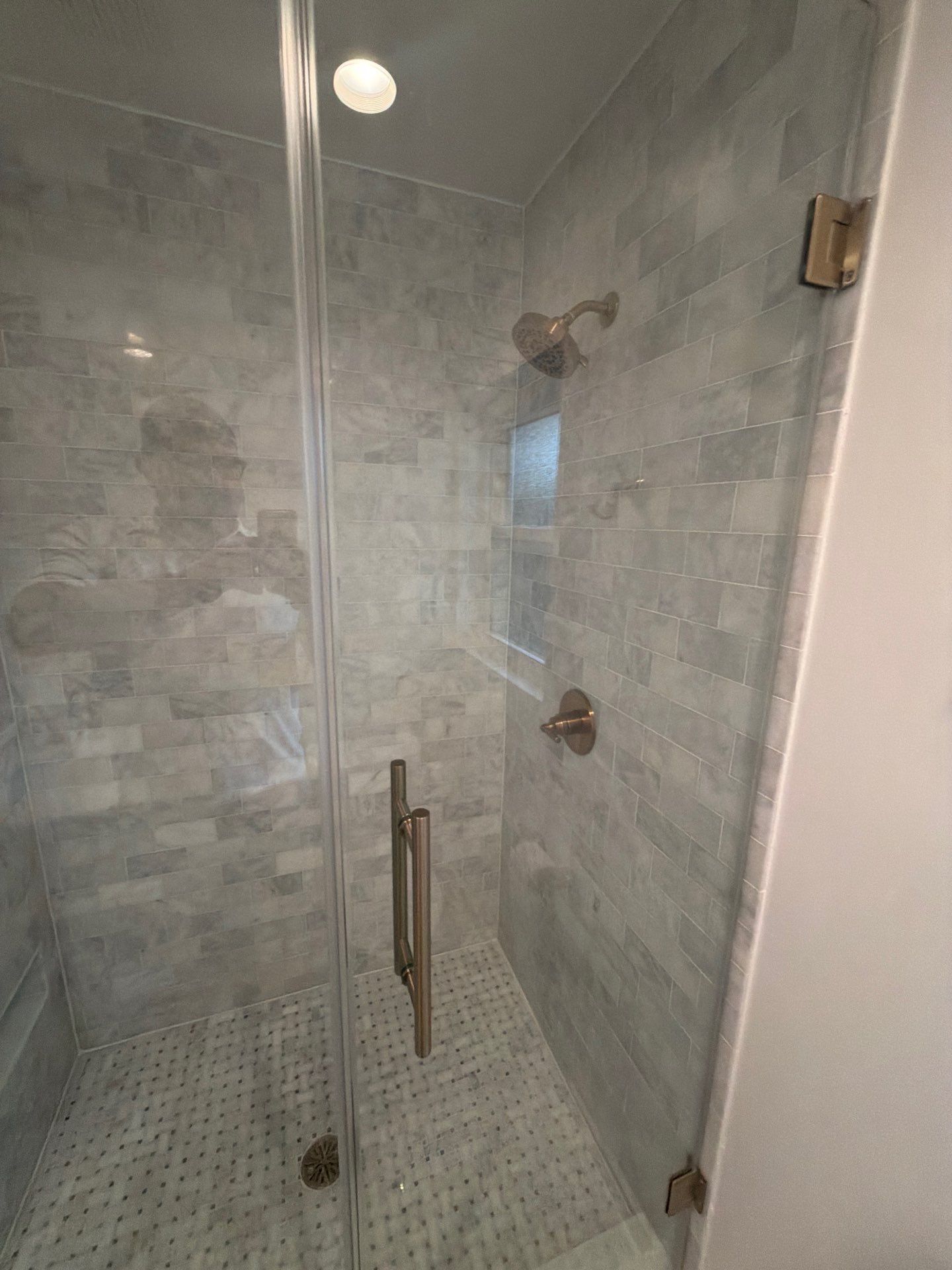 Modern glass shower stall with gray tile walls and mosaic floor, viewed from the bathroom.