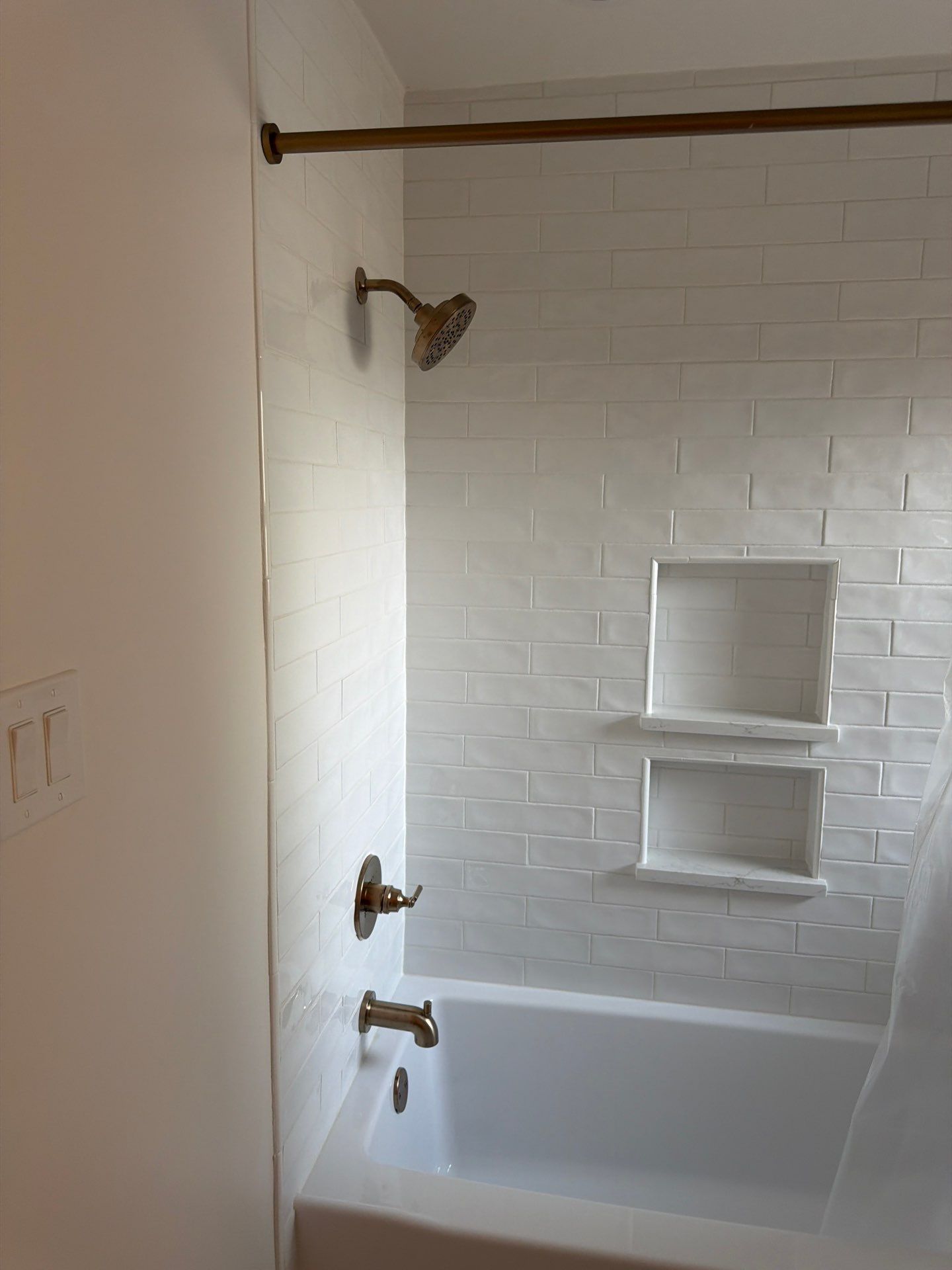 White-tiled bathtub and shower with built-in wall shelves and bronze fixtures in a bathroom