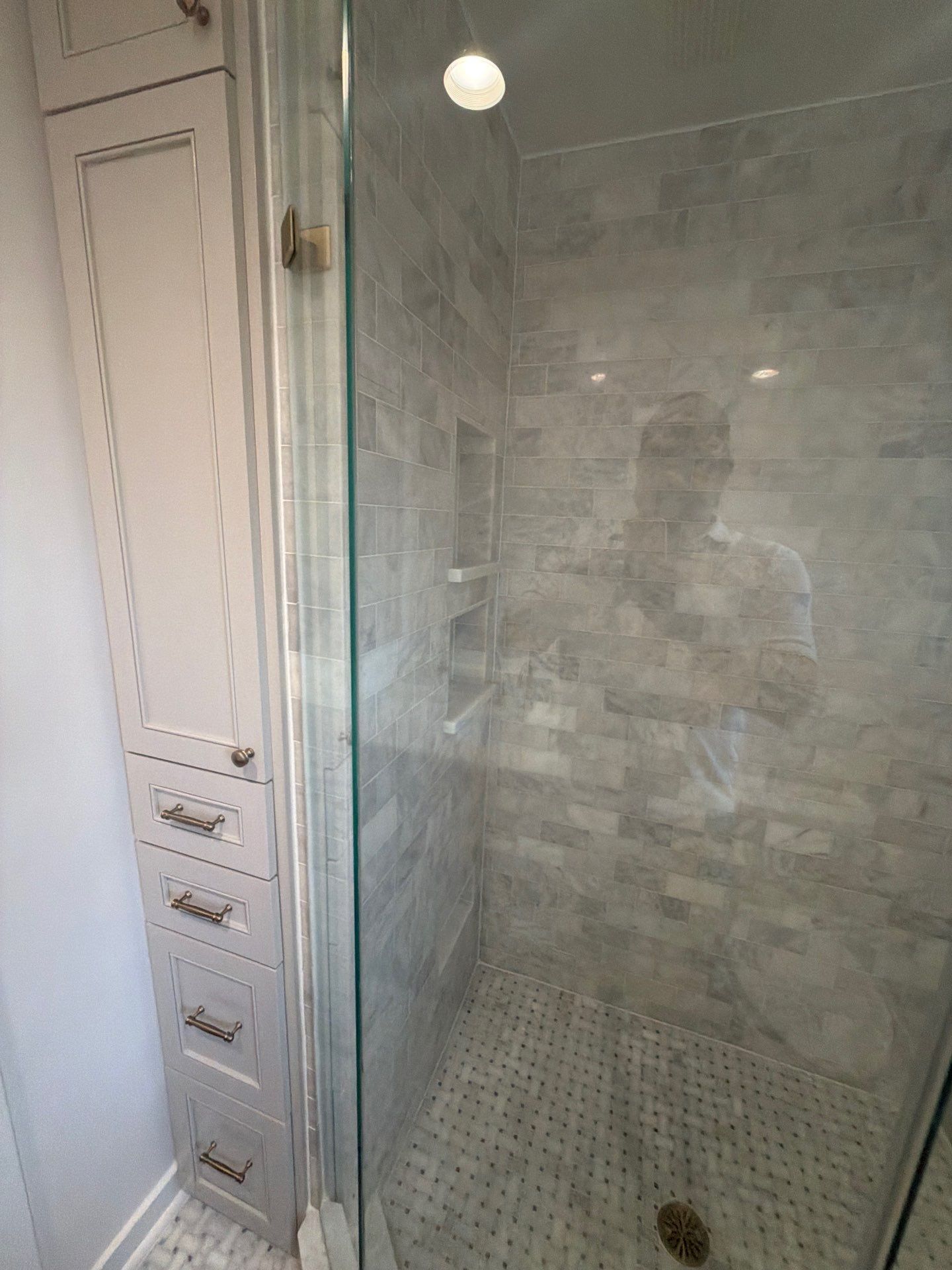 Bathroom shower stall with glass door, tiled walls, and built-in white drawers beside it