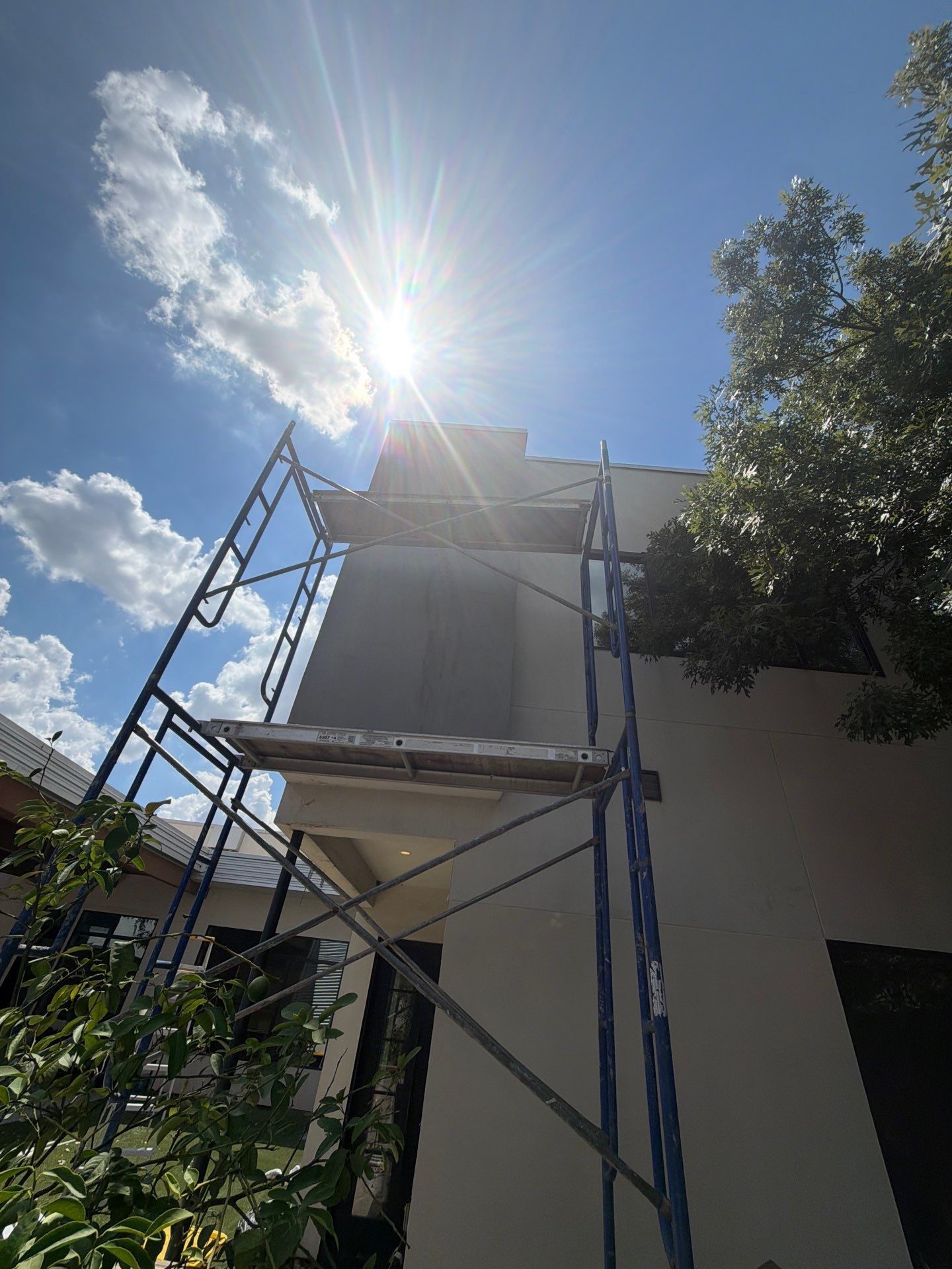 Blue scaffolding beside a white building under bright sun and blue sky