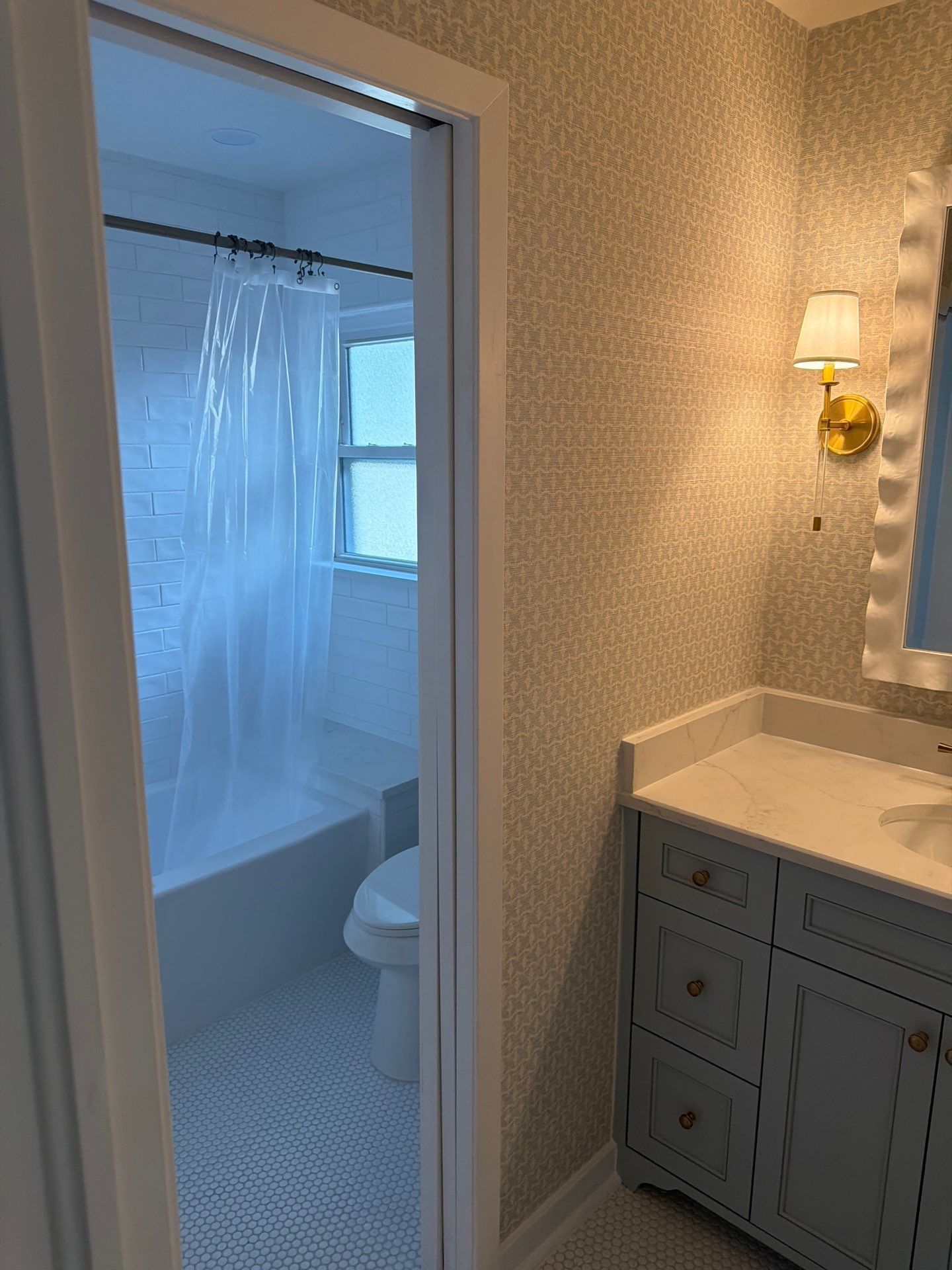 Bathroom vanity beside open doorway to a shower and toilet, with white and blue decor.