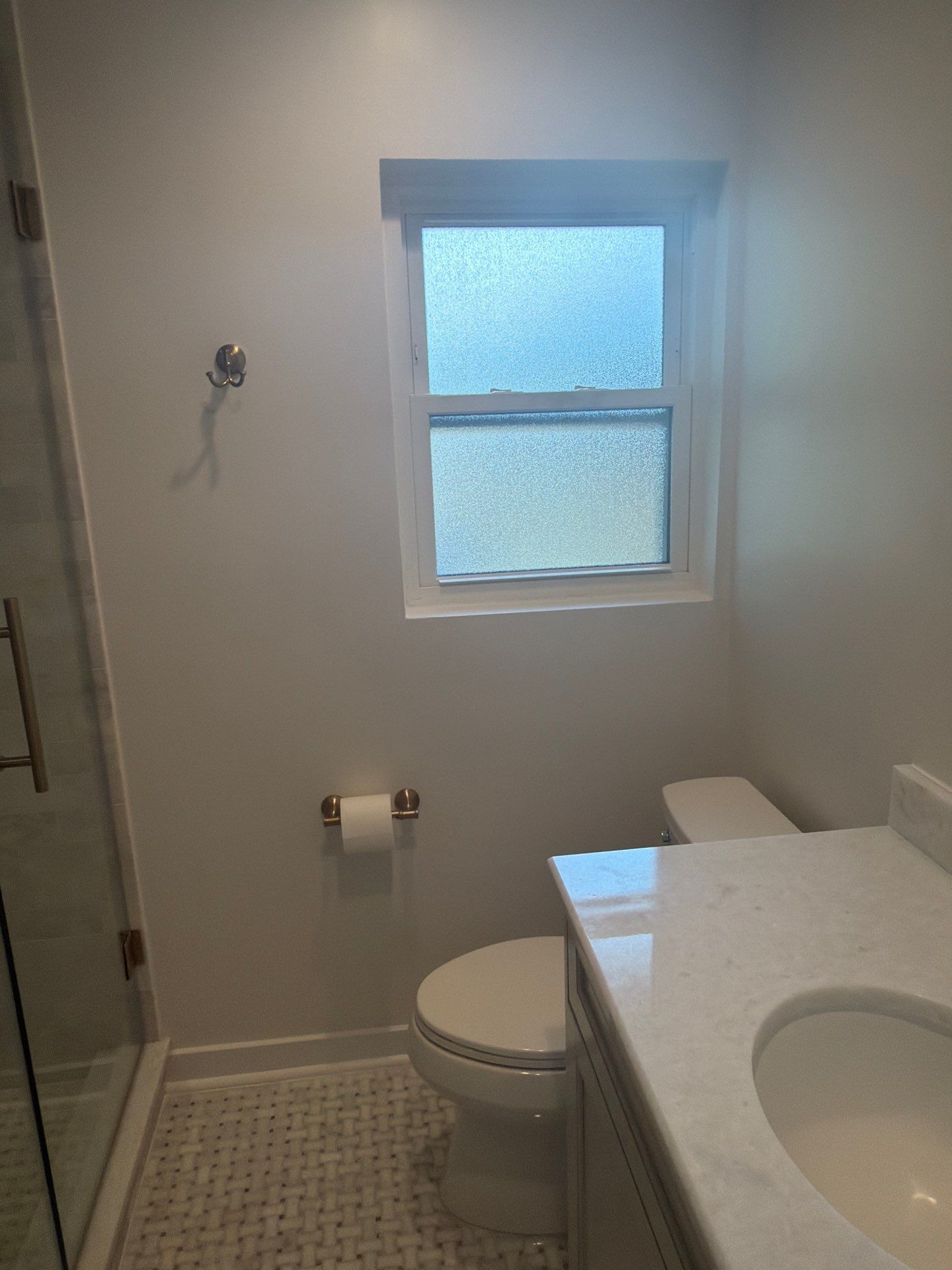 Small bathroom with toilet, sink counter, frosted window, and shower on the left.