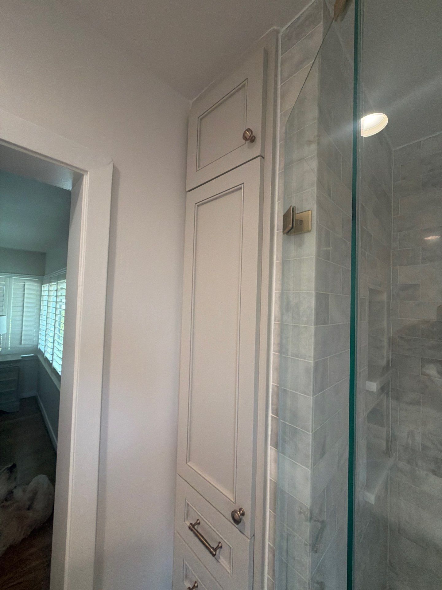 Bathroom vanity with white cabinets, mirror, and glass shower door in a narrow hallway