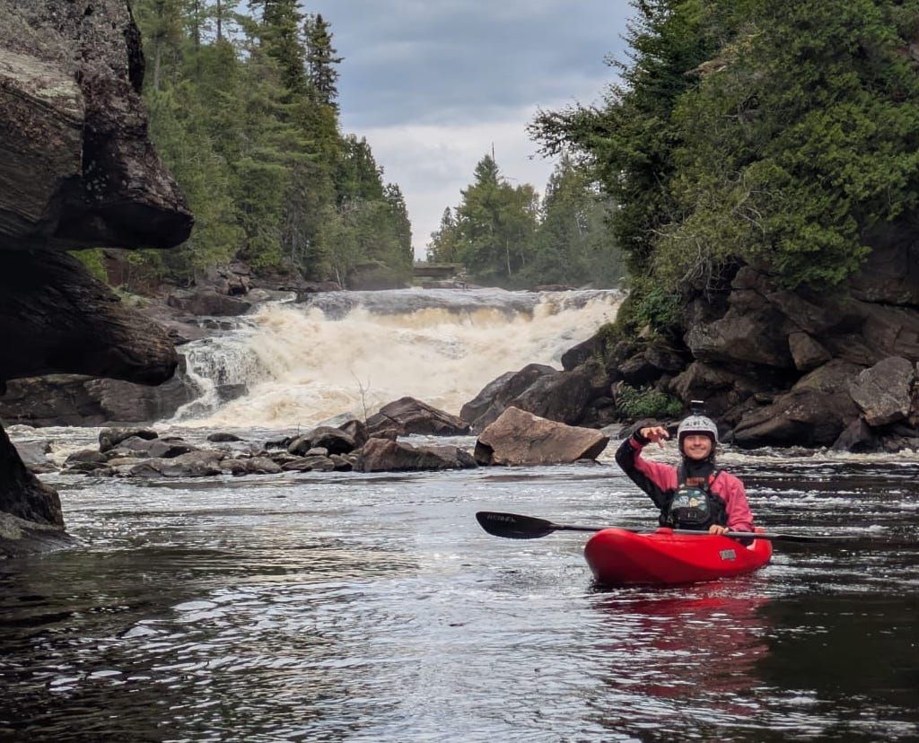 Kayaker in a red boat below a waterfall