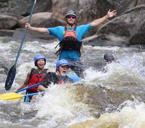 Paddler standing with arms raised behind seated rafters