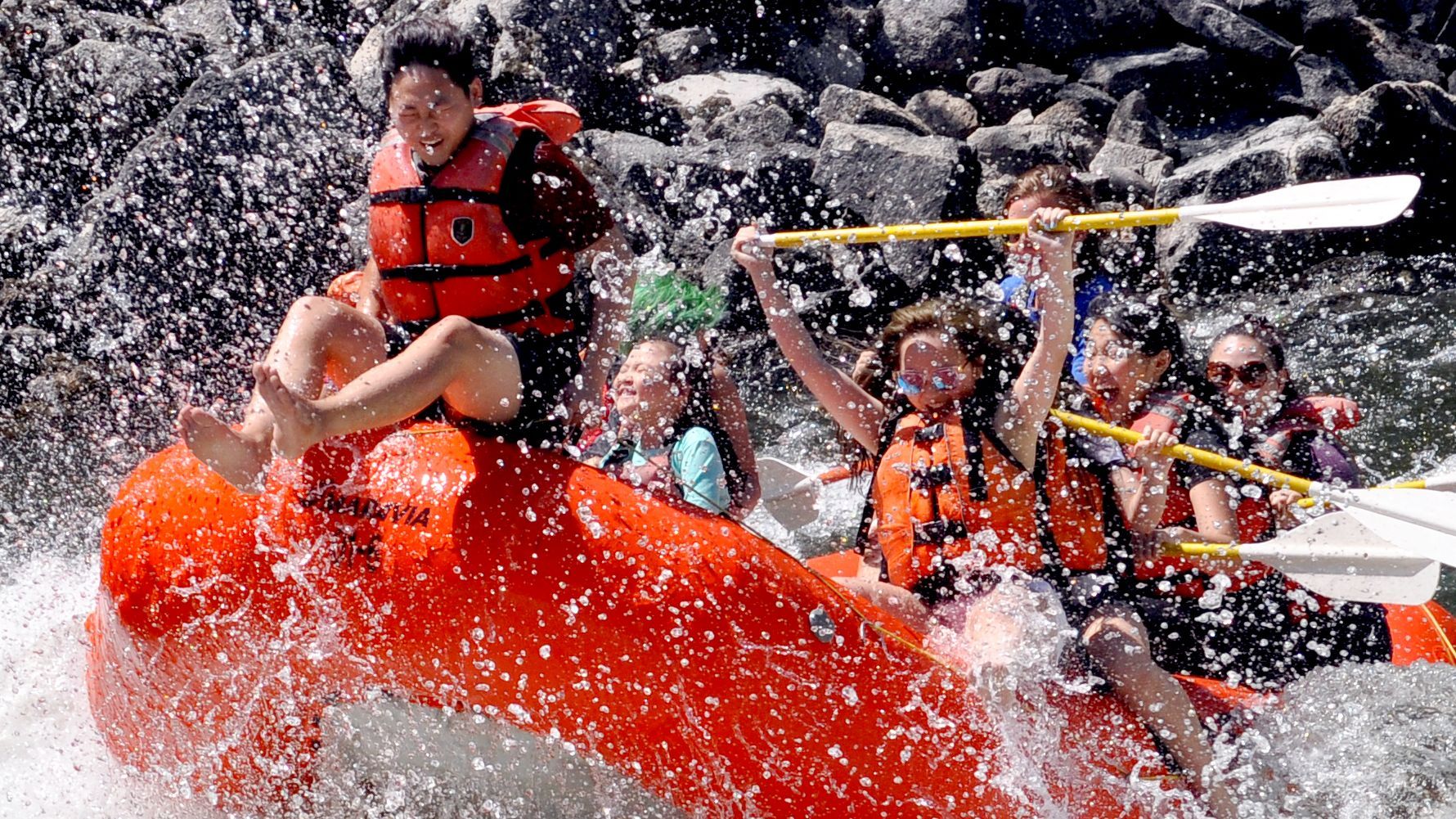 Whitewater splashing over rafters in an orange raft