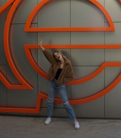 Staff member posing beside a large orange circular sign