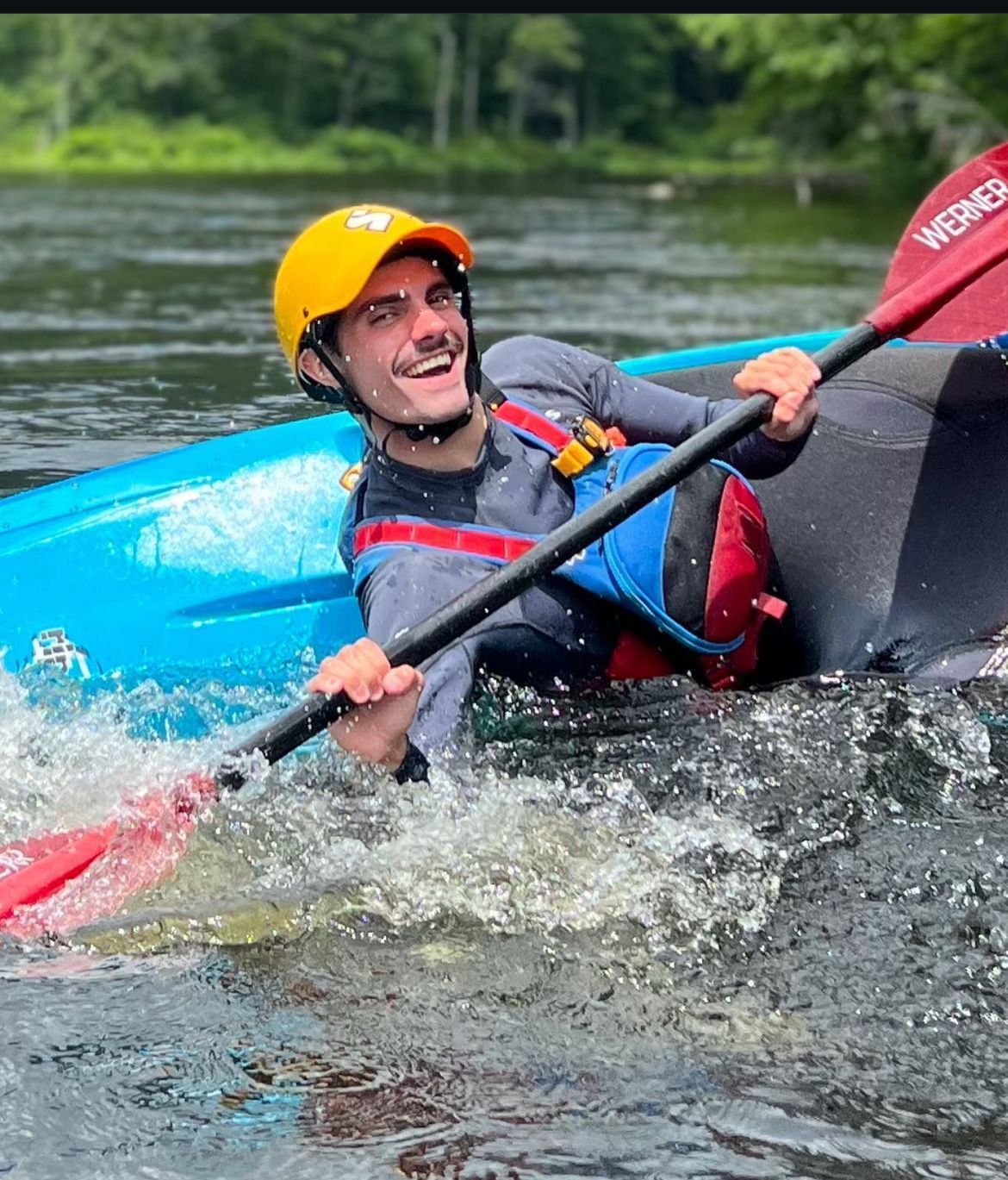 Smiling kayaker wearing a yellow helmet on a river