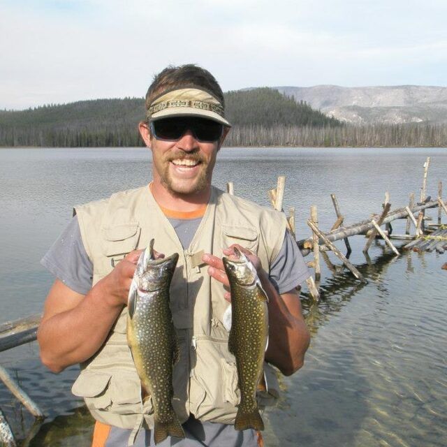 Staff member smiling beside a lake and mountains