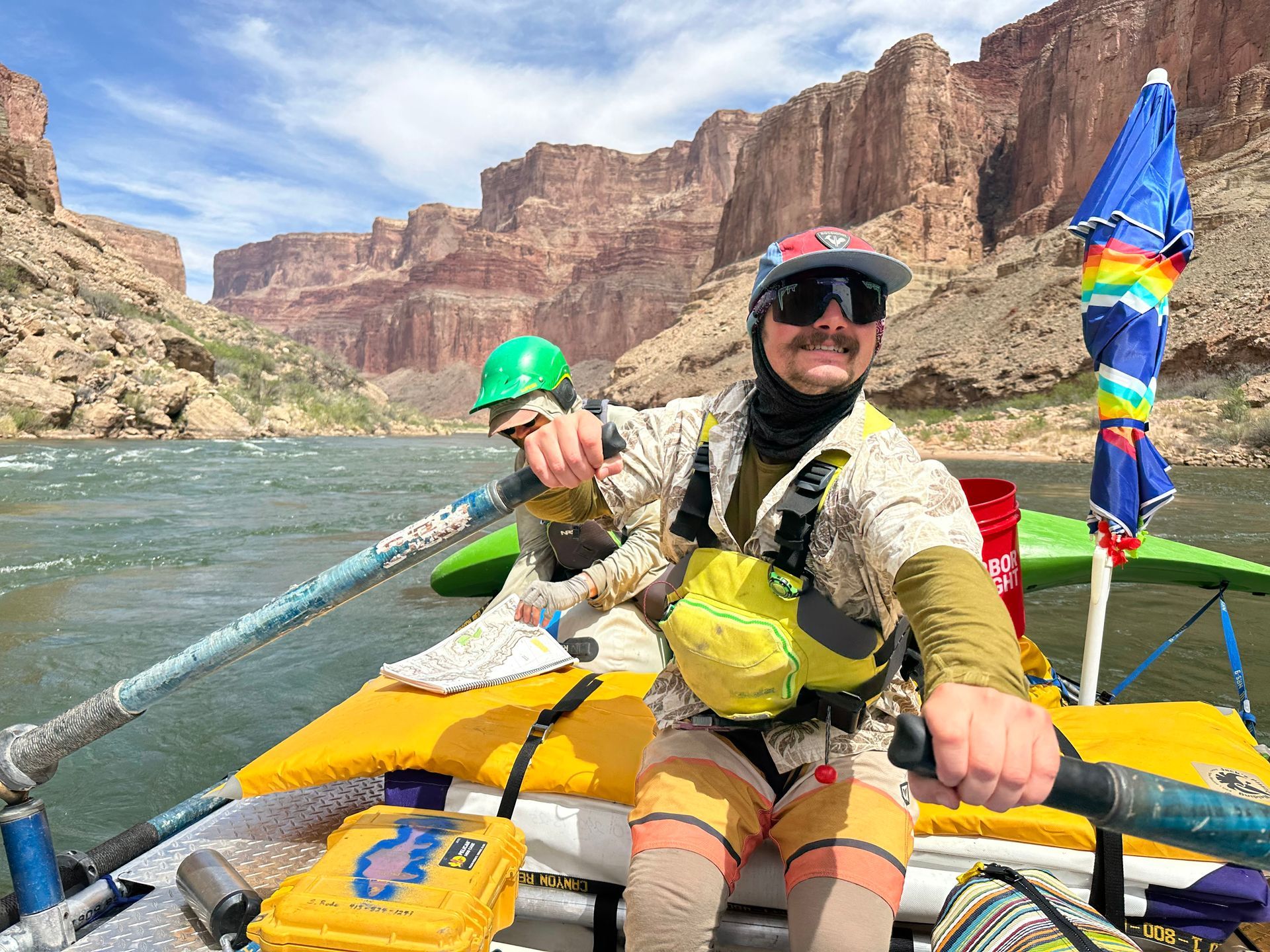 Helmeted rafters on a river through a red rock canyon