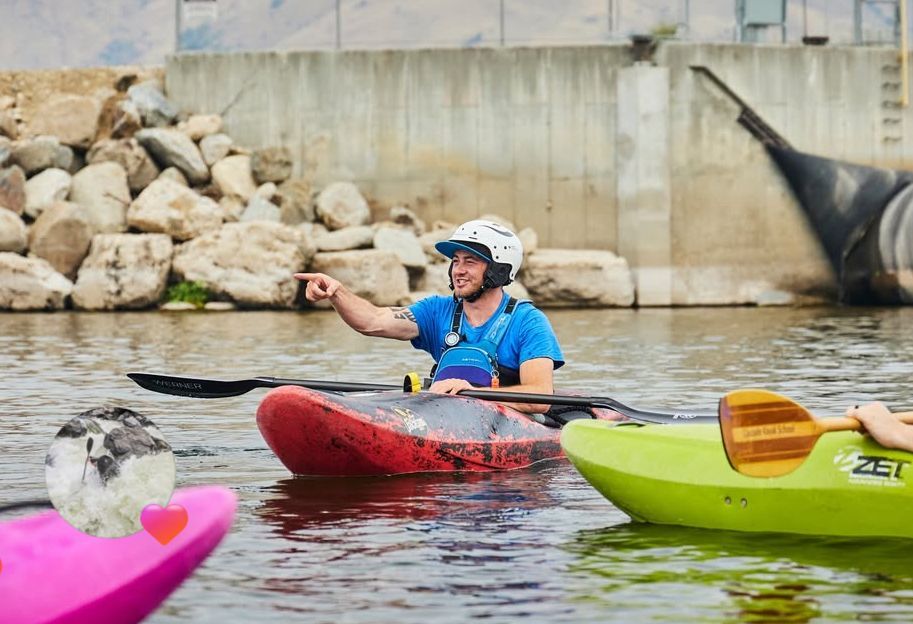 Kayakers in colorful boats beside a concrete bridge